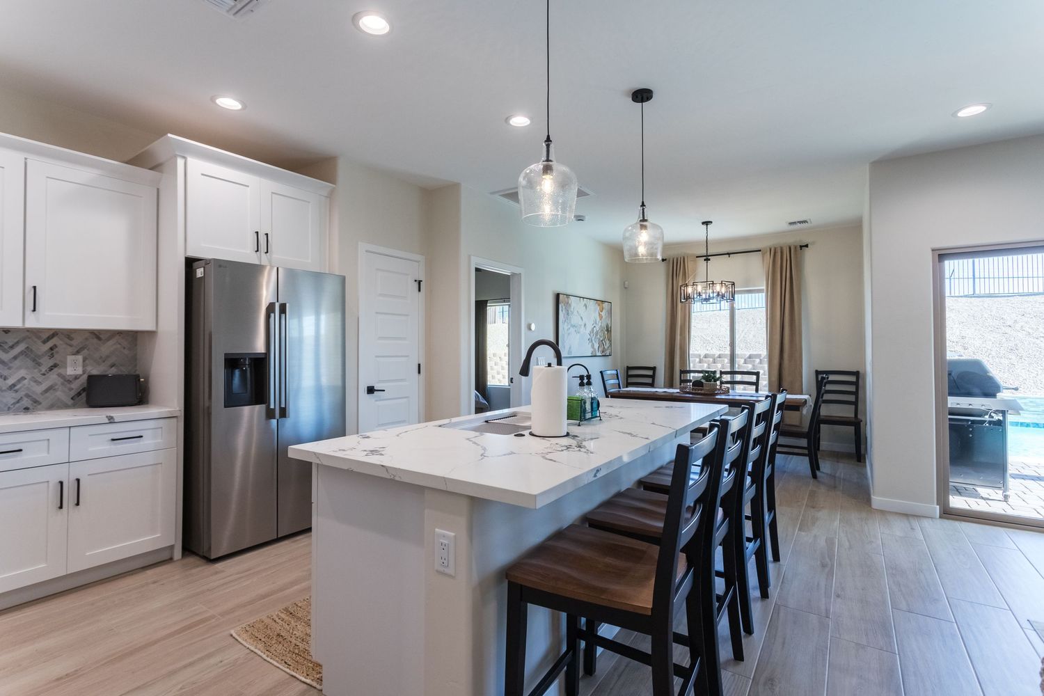 Modern open concept kitchen features white cabinets, stainless appliances, and dark island with pendant lighting.