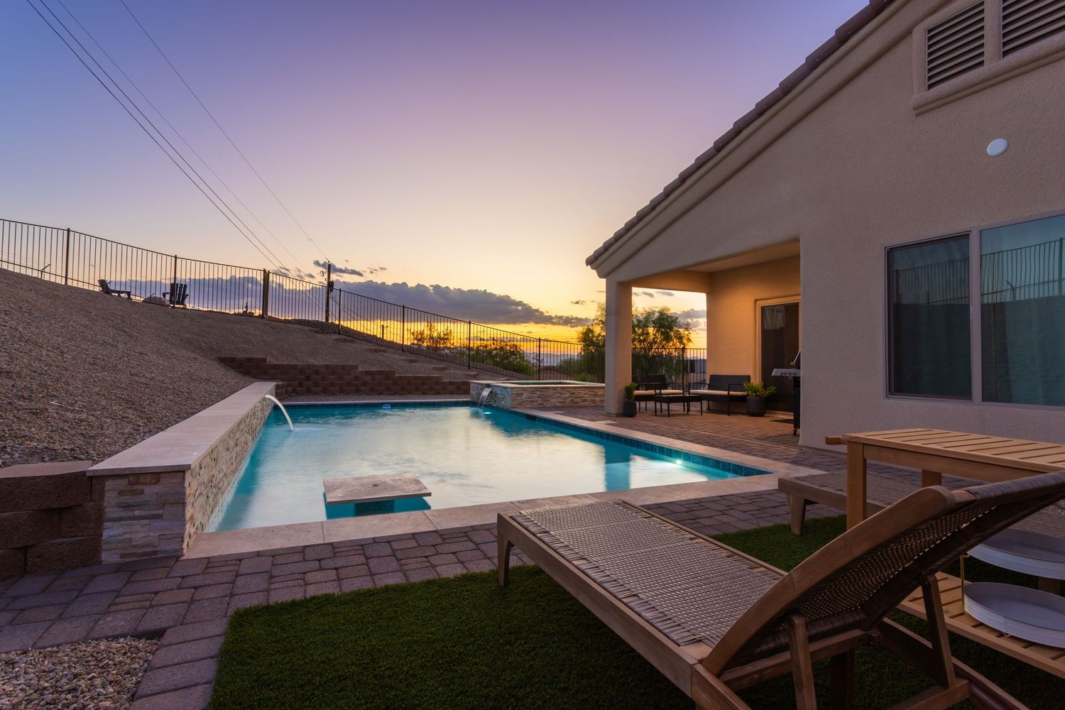 Modern infinity pool with geometric design overlooks desert landscape during vibrant sunset.