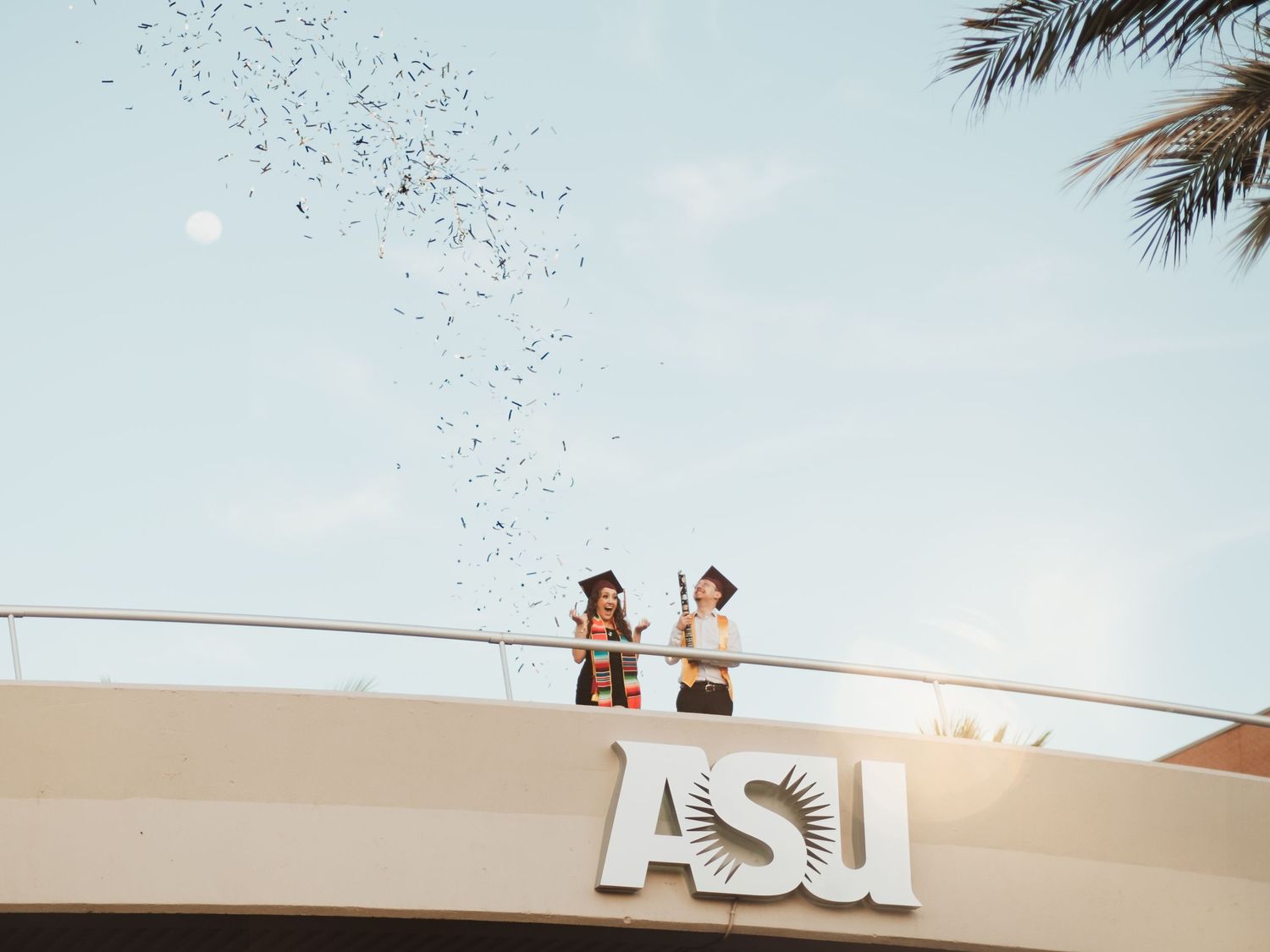 Graduates celebrate on ASU sign with confetti flying in the air.