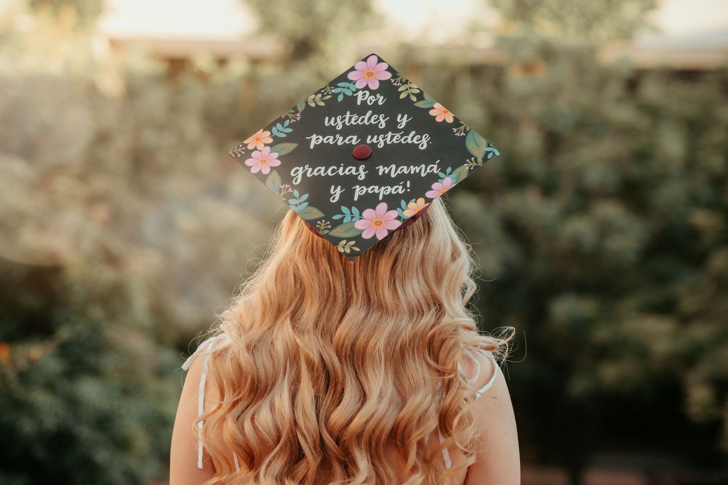 Decorated graduation cap with floral design shown from behind on blonde wavy hair.