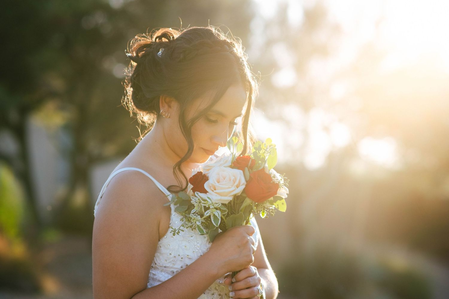 A bride holding her bouquet in soft golden sunlight during sunset.
