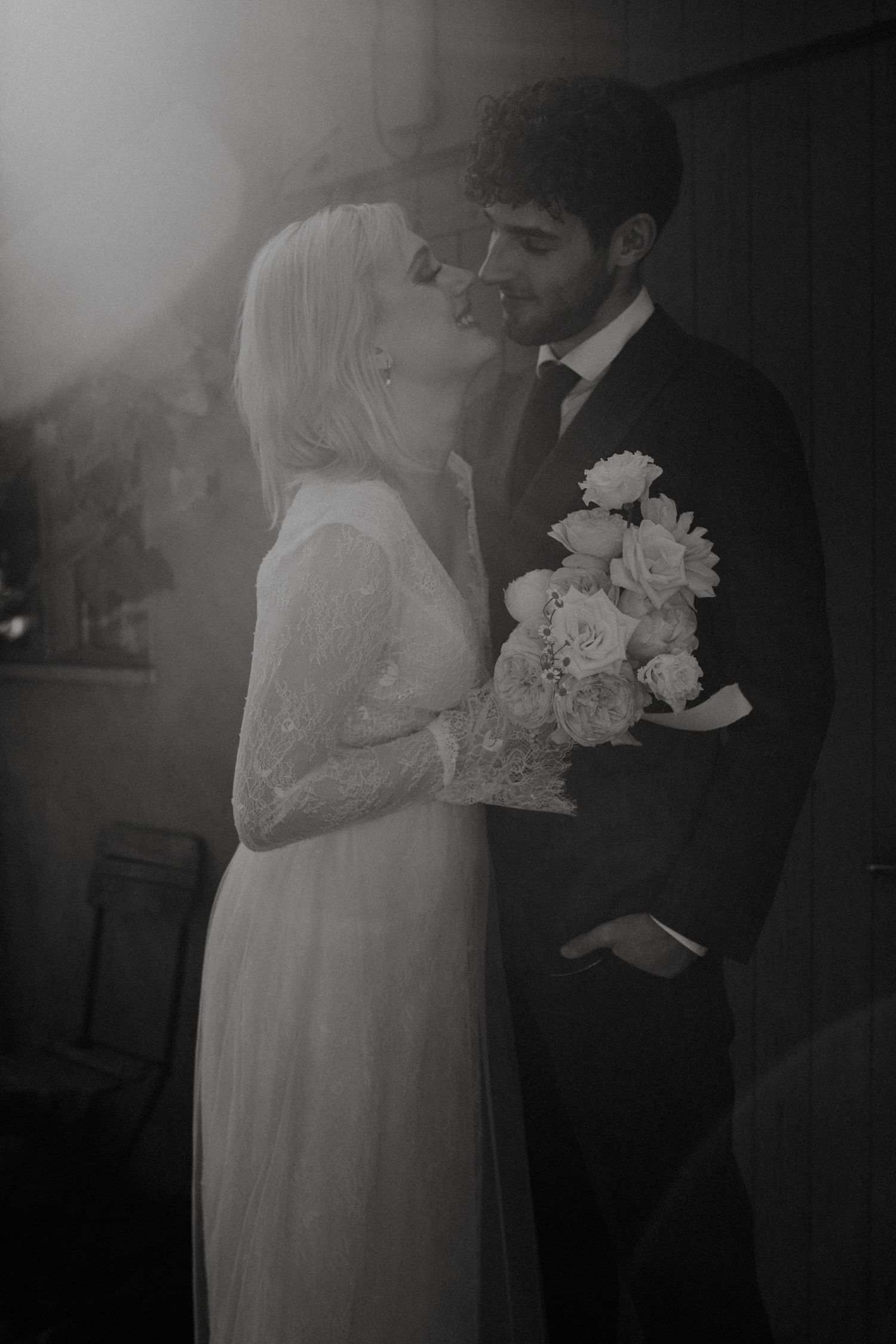A romantic black and white wedding photo showing a couple embracing while the bride holds a white floral bouquet.