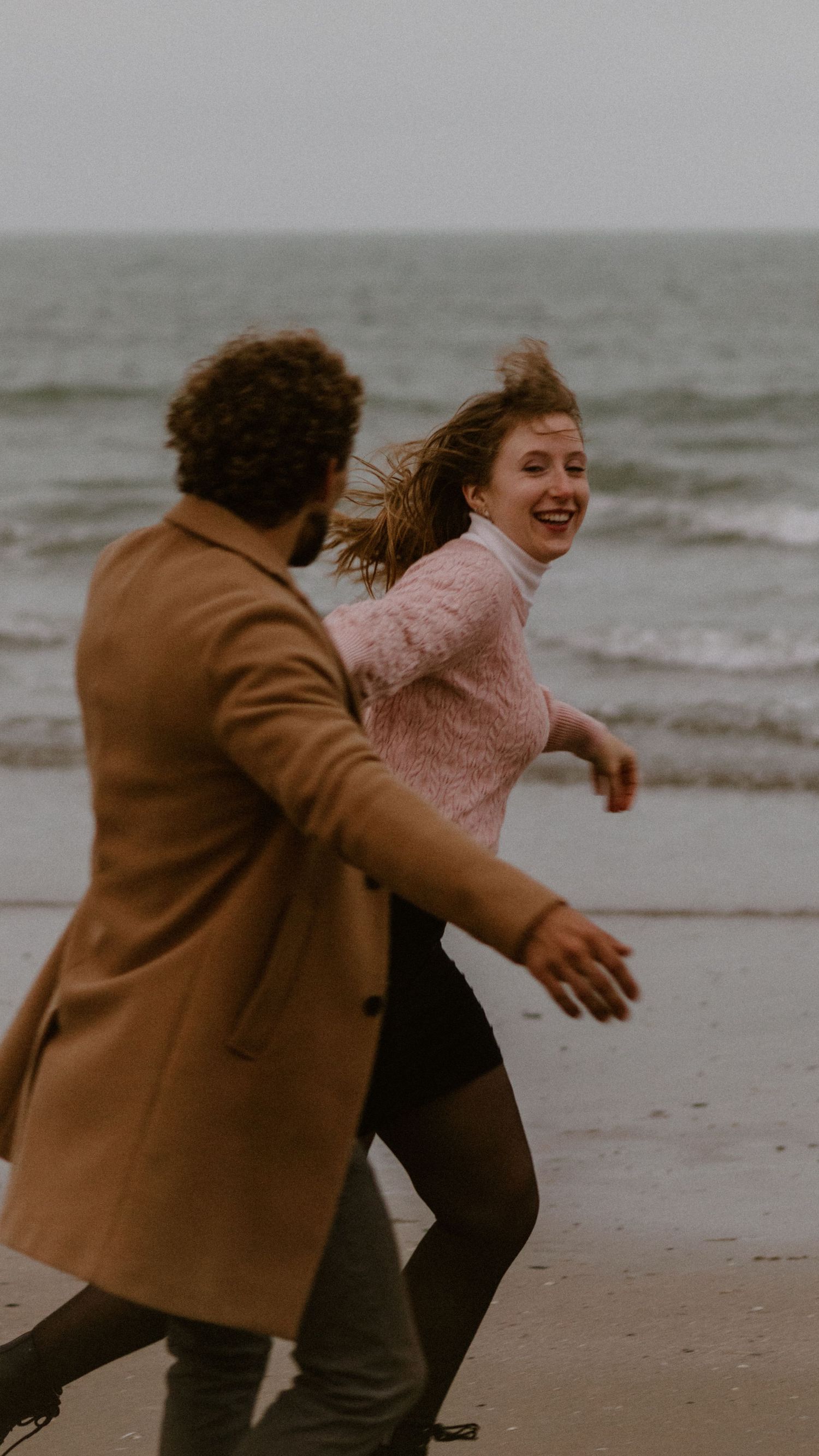 Een vrolijk koppel danst en lacht samen op een bewolkt strand.
