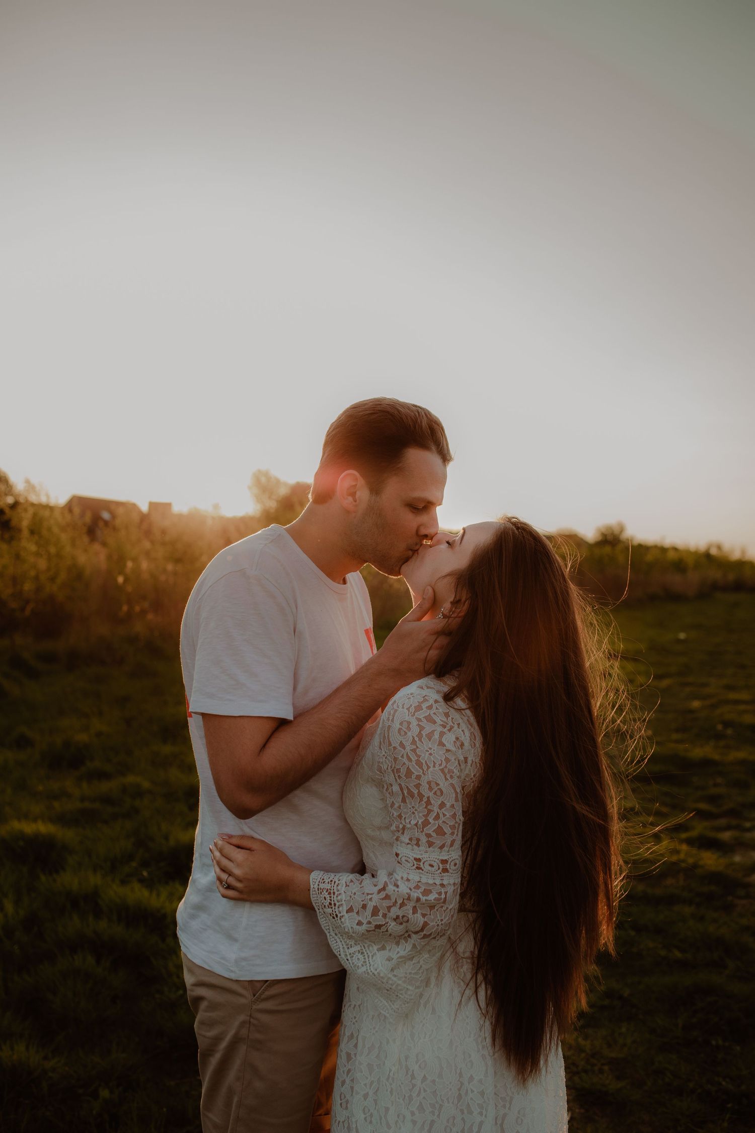 A romantic couple embraces and kisses in a sunlit field during golden hour, creating a dreamy silhouette against nature.