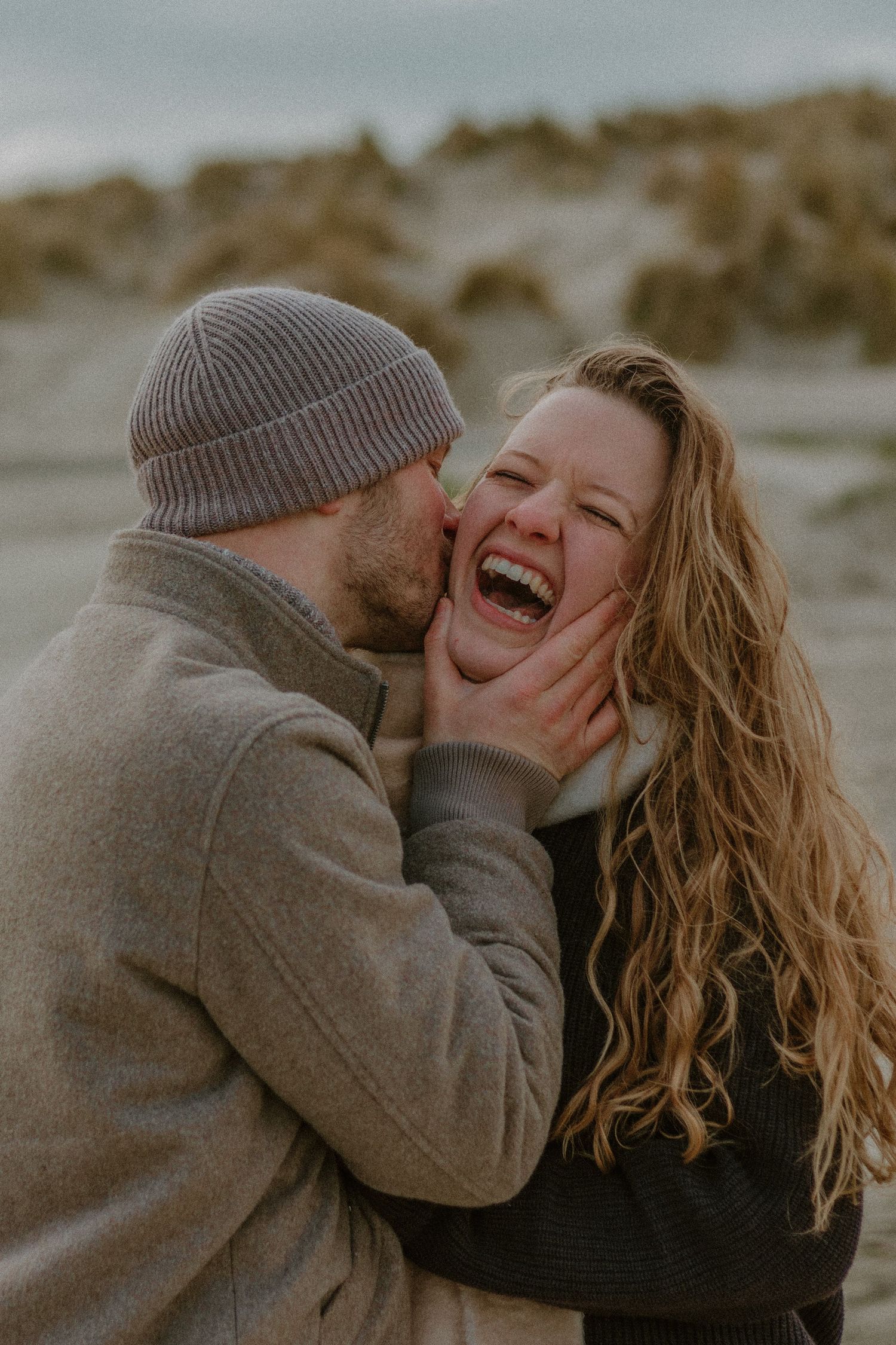A couple shares joyful laughter together during an intimate outdoor photoshoot in muted tones.