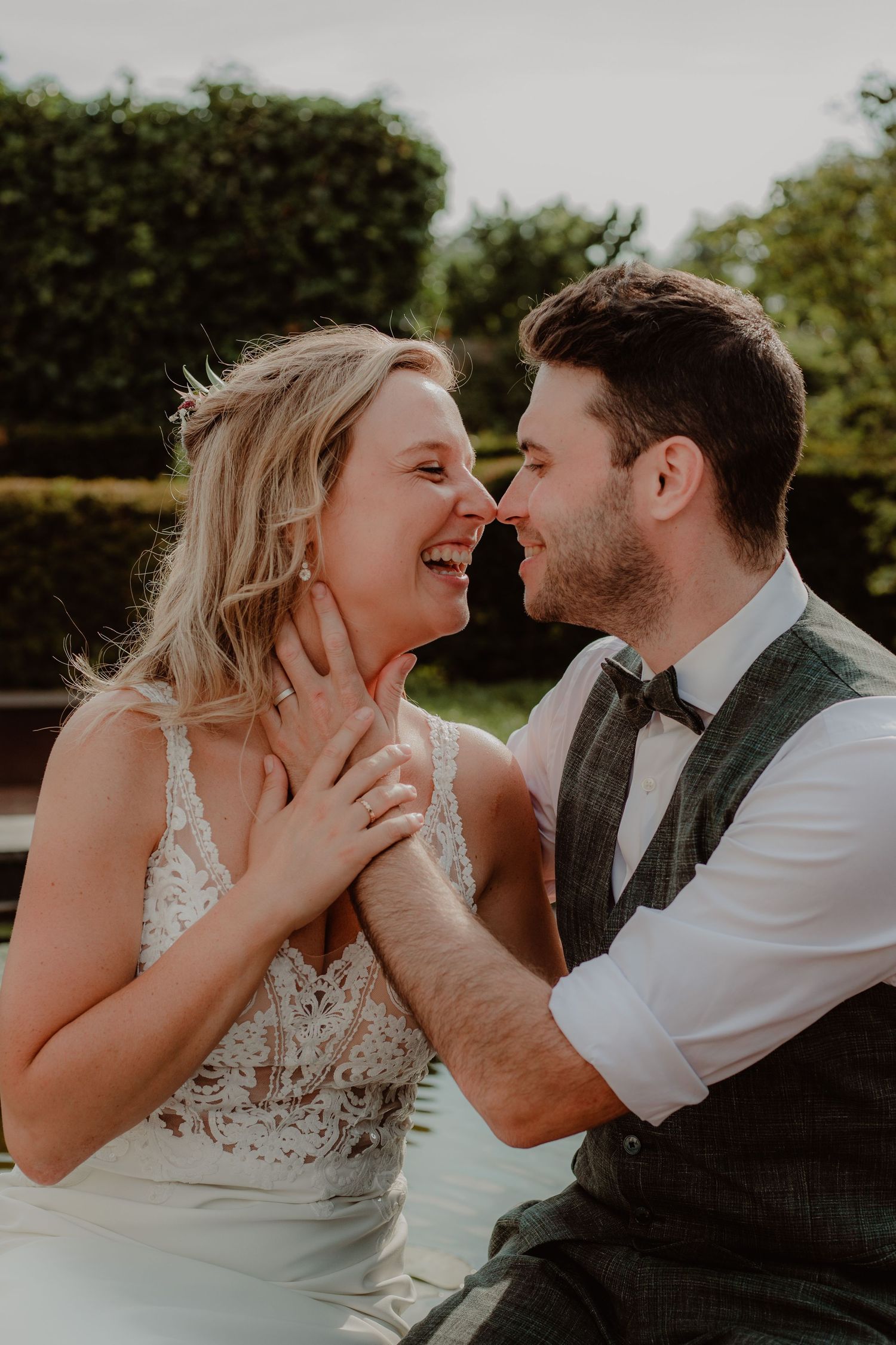 A joyful couple shares an intimate moment of laughter during their wedding photoshoot in a garden setting.