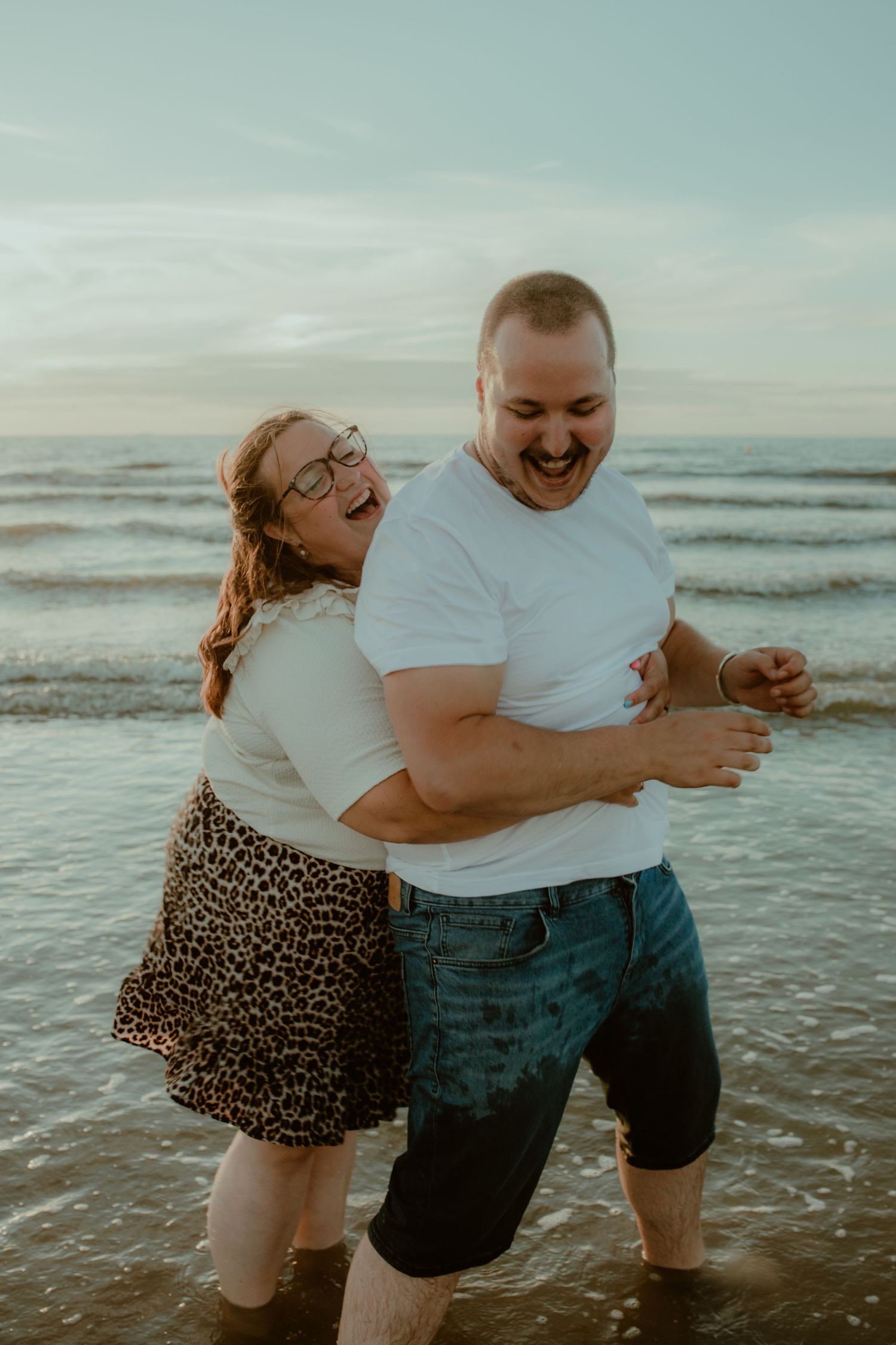 A couple shares joyful moments together on a beach at sunset, playing and laughing in the ocean waves.