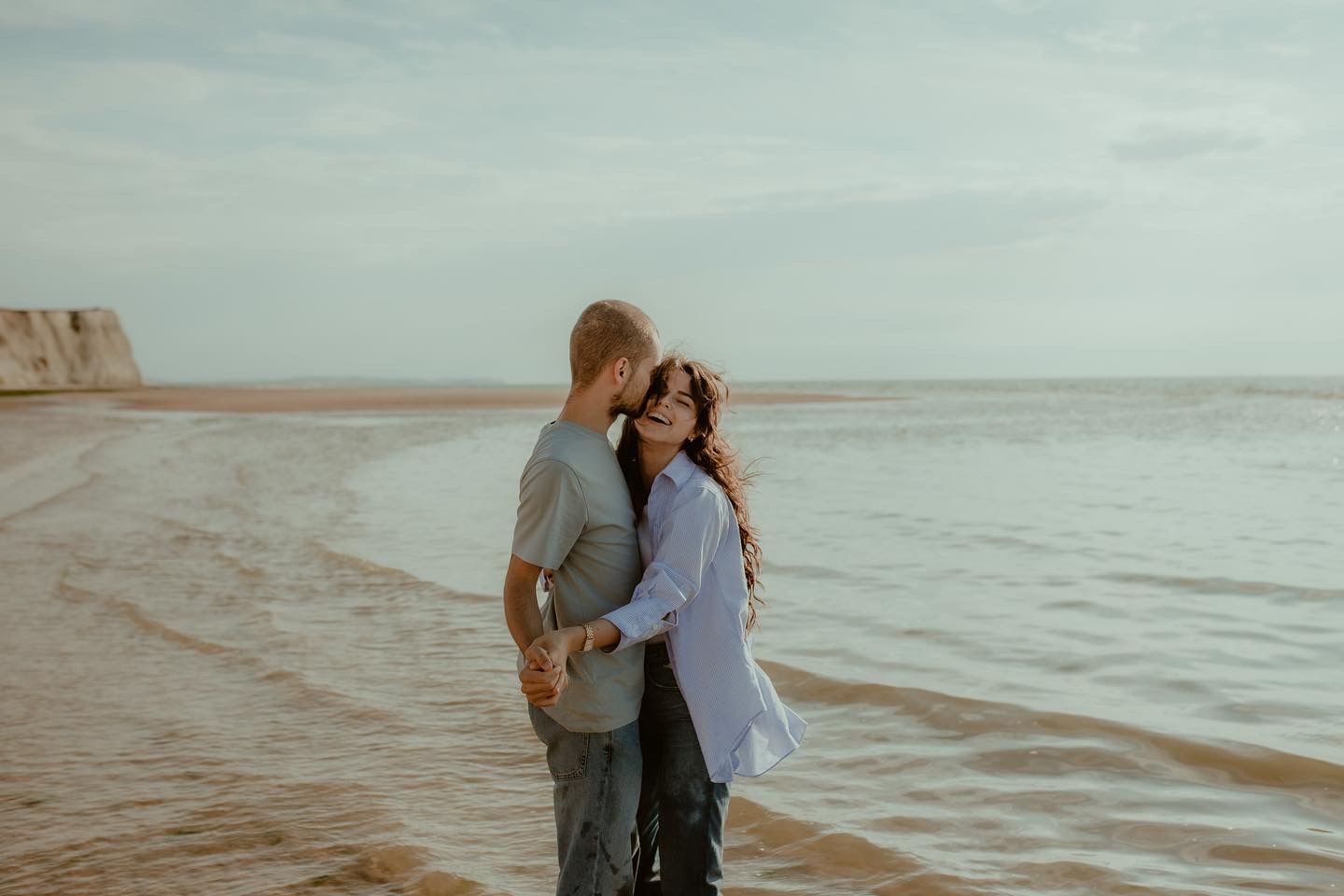Romantic couple embraces on misty beach at sunset creating silhouette against serene ocean backdrop.