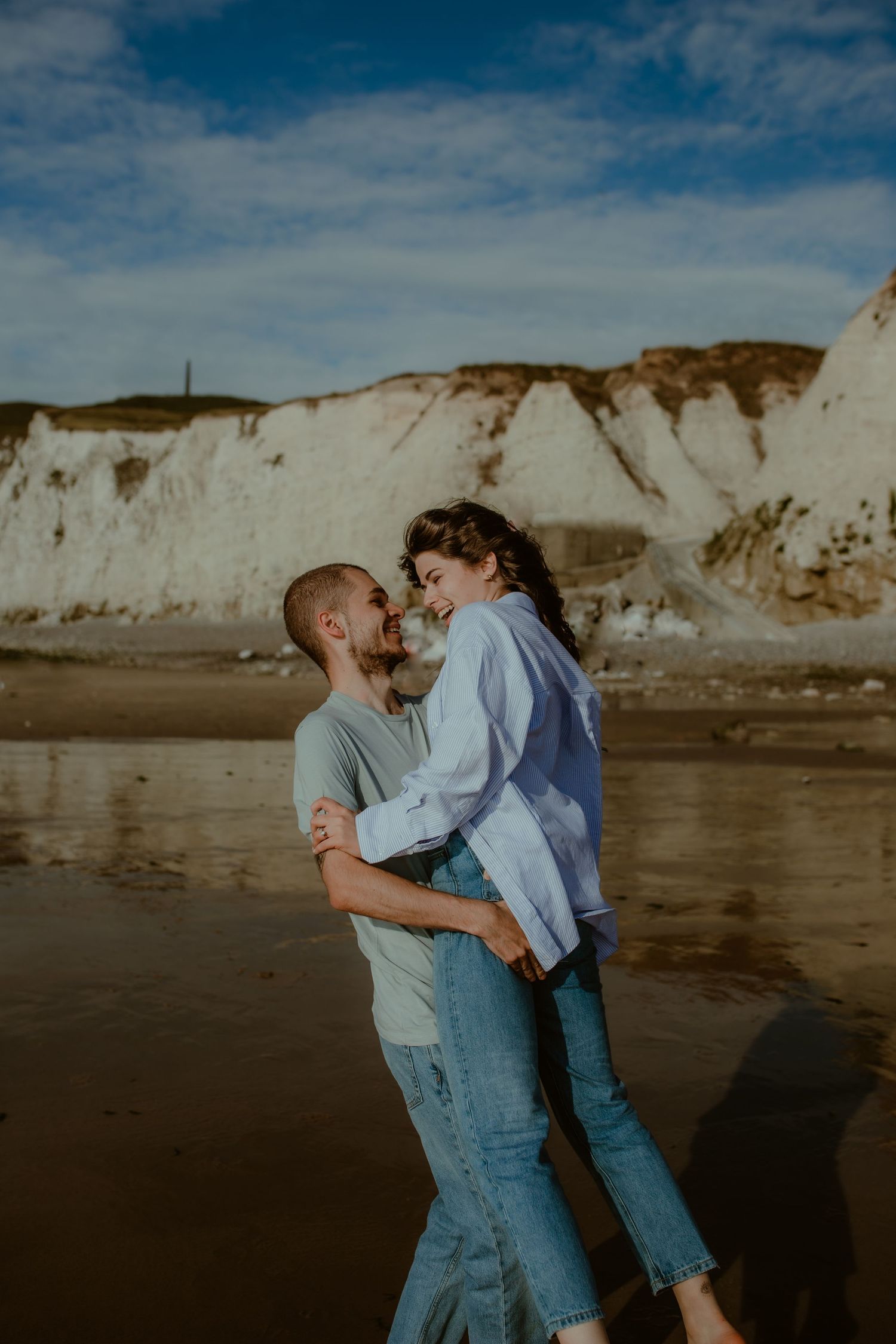 A couple shares an intimate moment together on a beach with white cliffs in the background at sunset.