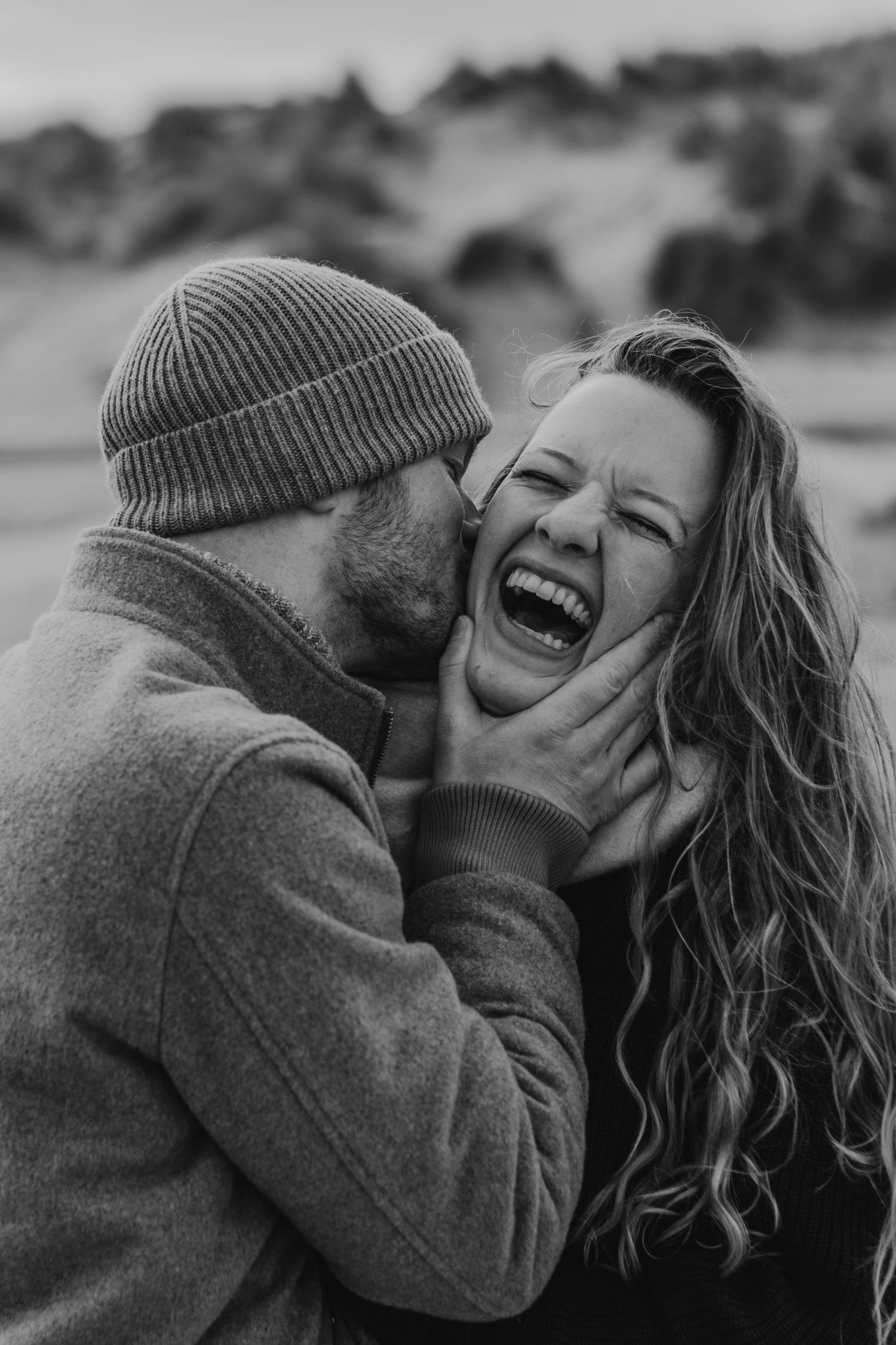 A joyful couple shares an intimate black and white moment while wearing cozy winter sweaters and beanies.