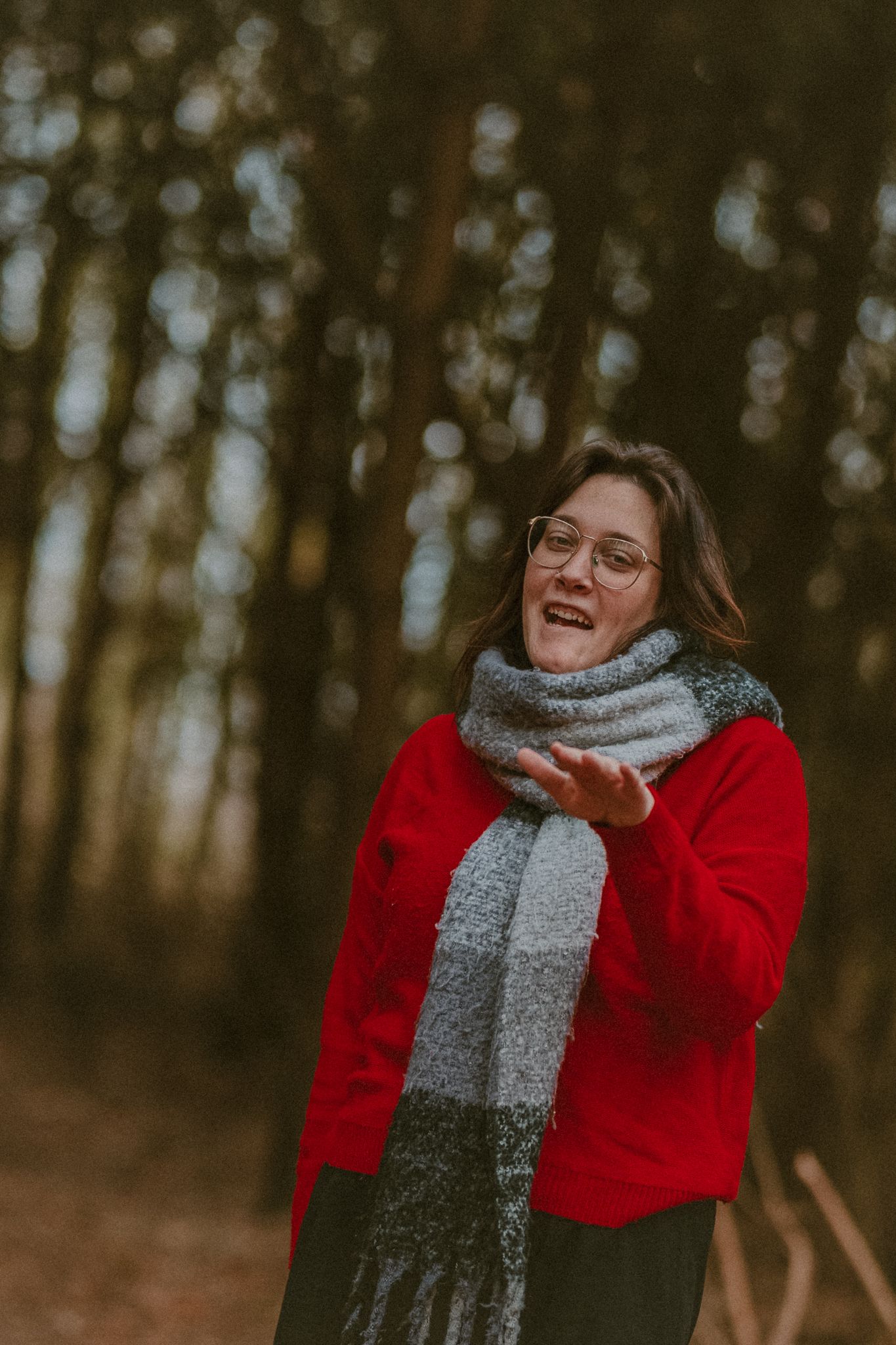 A joyful moment captured in a forest wearing a red sweater, gray scarf and expressing happiness in autumn weather.