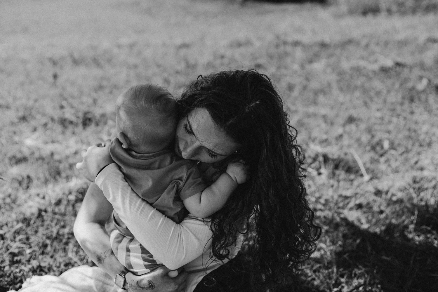 Black and white photo of a mother tenderly holding her baby outdoors on grass.
