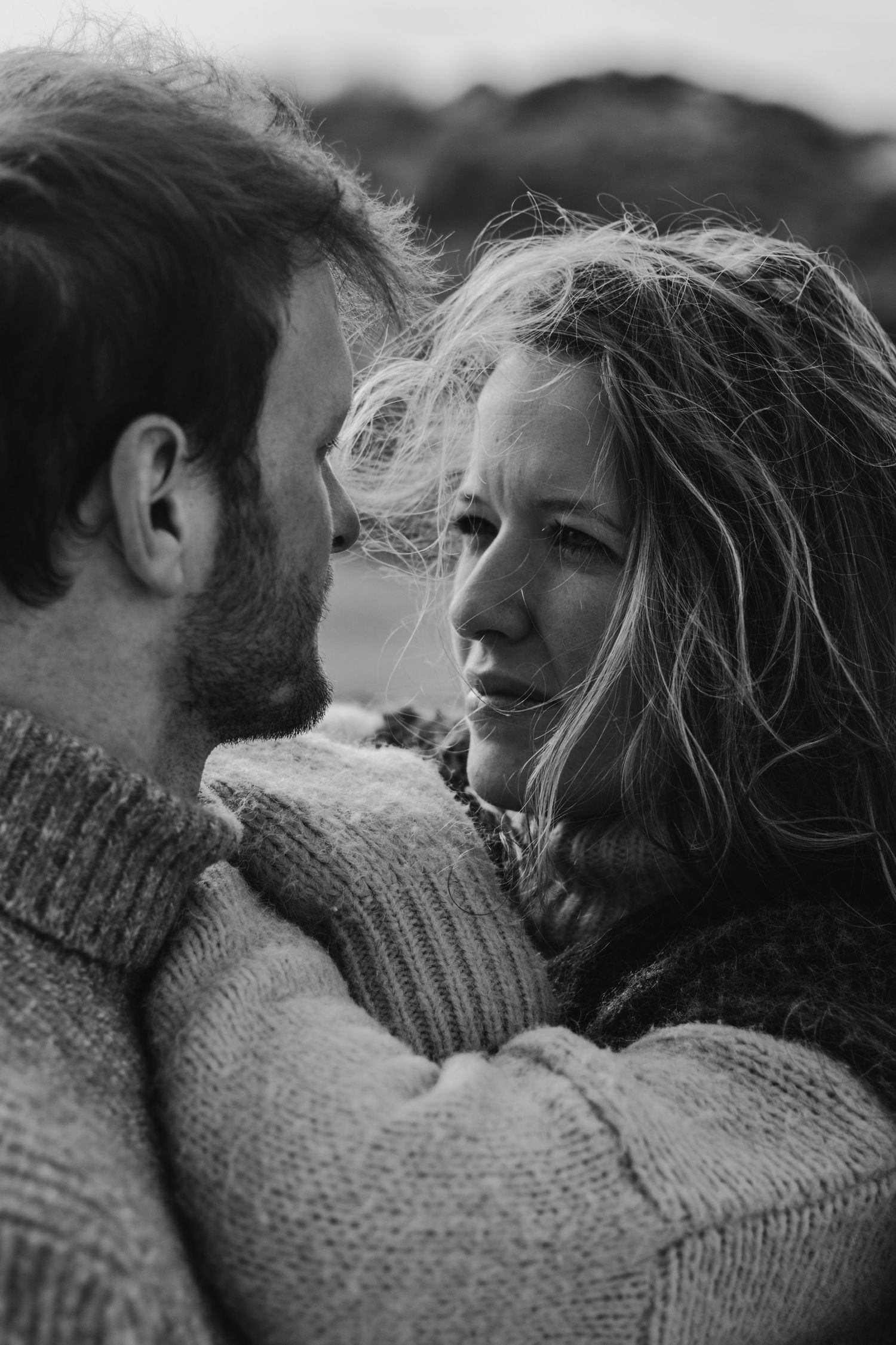 Intimate black and white portrait of couple in cozy sweaters sharing a tender moment outdoors.