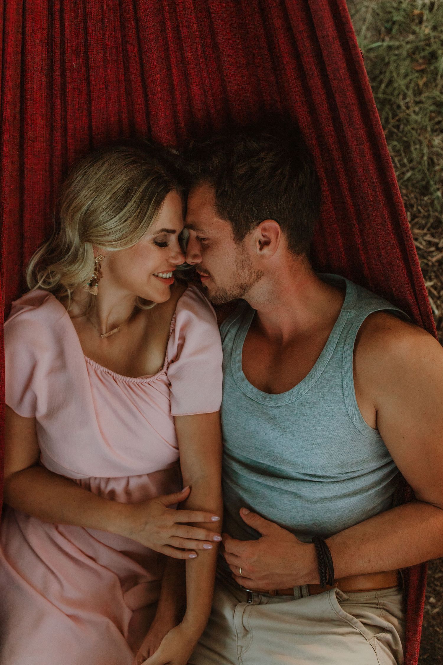 Romantic couple sharing an intimate moment while lying together on a red hammock outdoors.