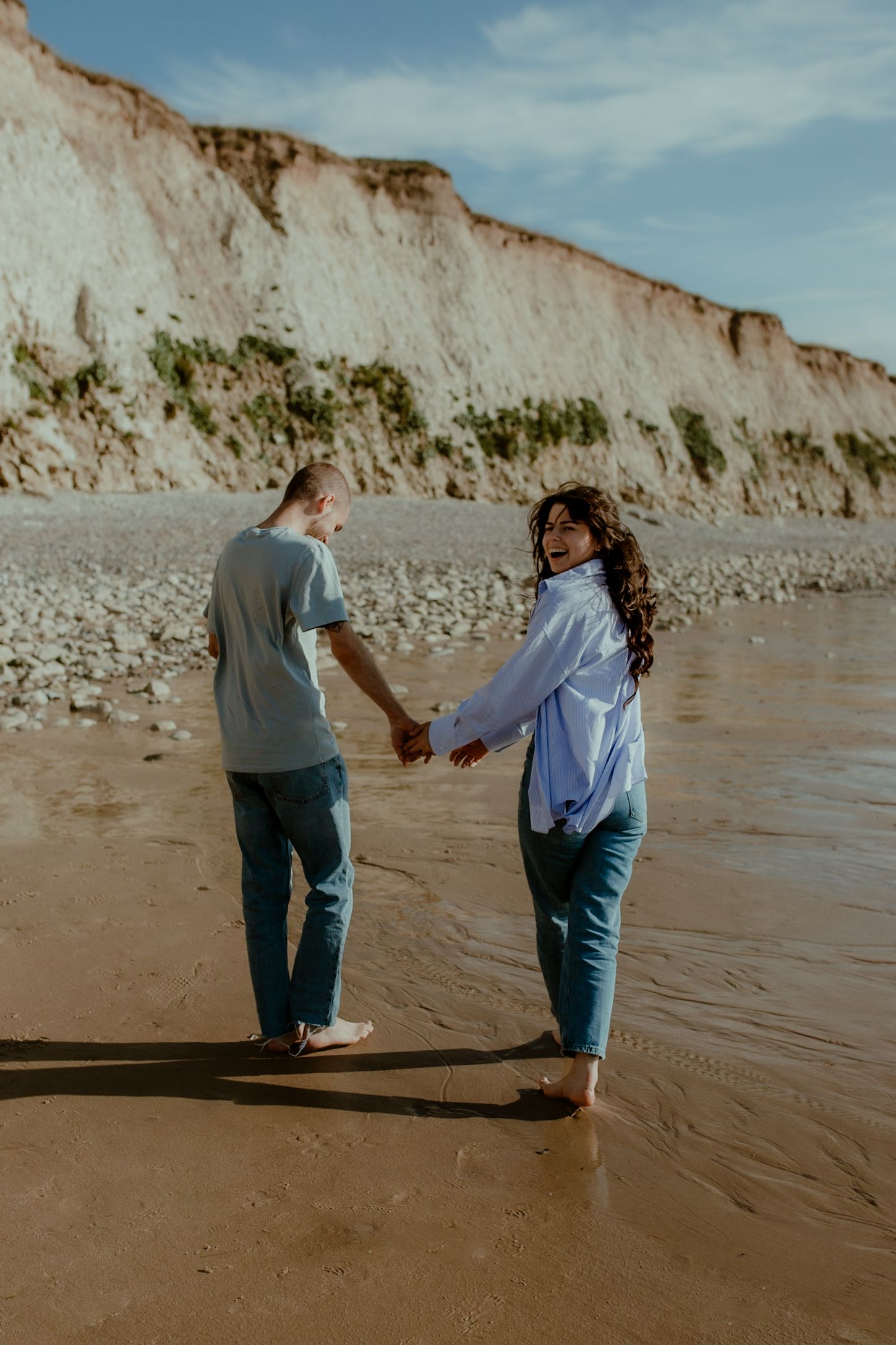 Two people walking along a sandy beach with white cliffs in the background on a sunny day.