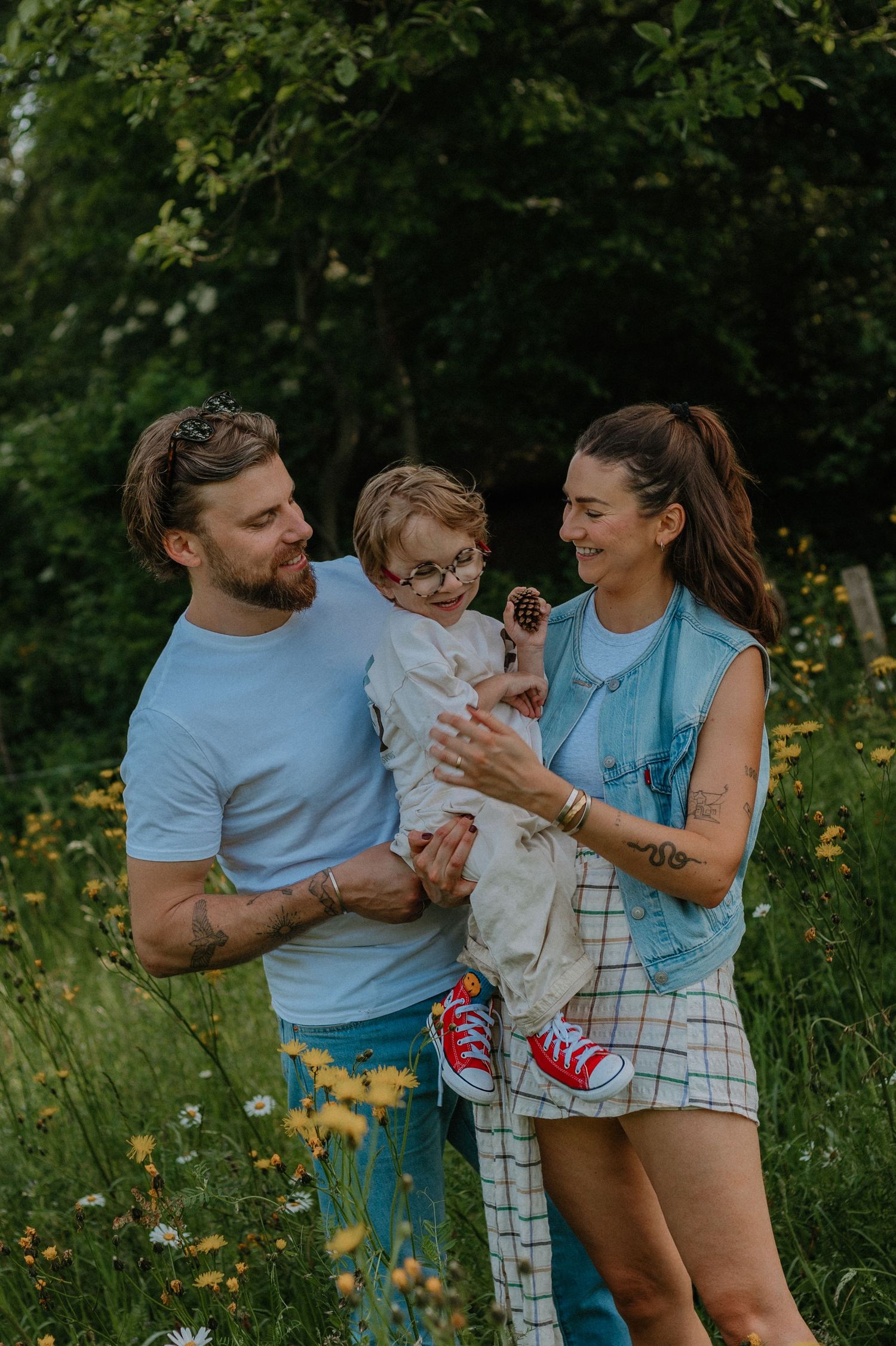 A happy family with a young child wearing glasses enjoys a sunny day in a lush green meadow with wildflowers.