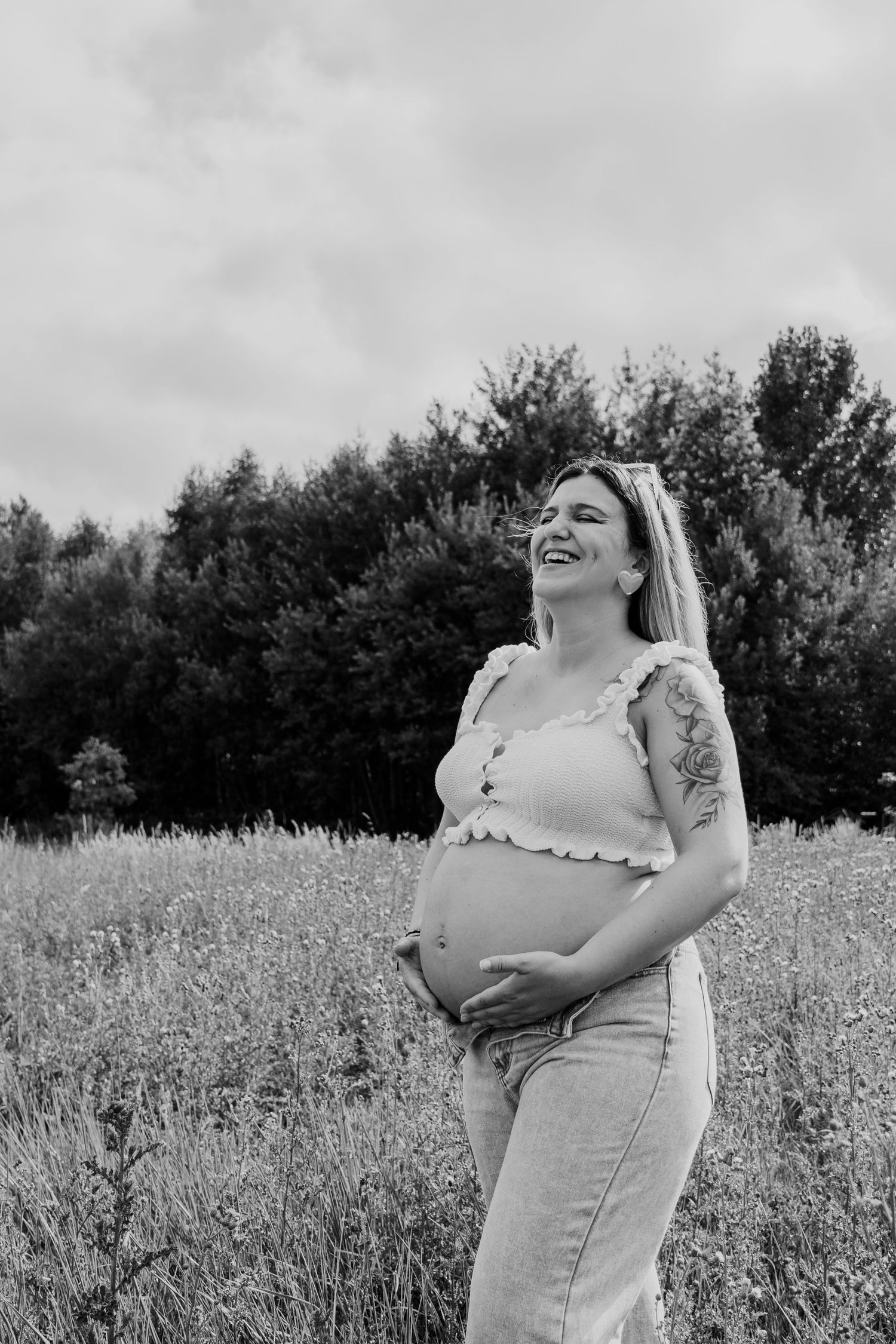 Black and white maternity photos show a joyful moment in a wildflower meadow with natural sunlight.