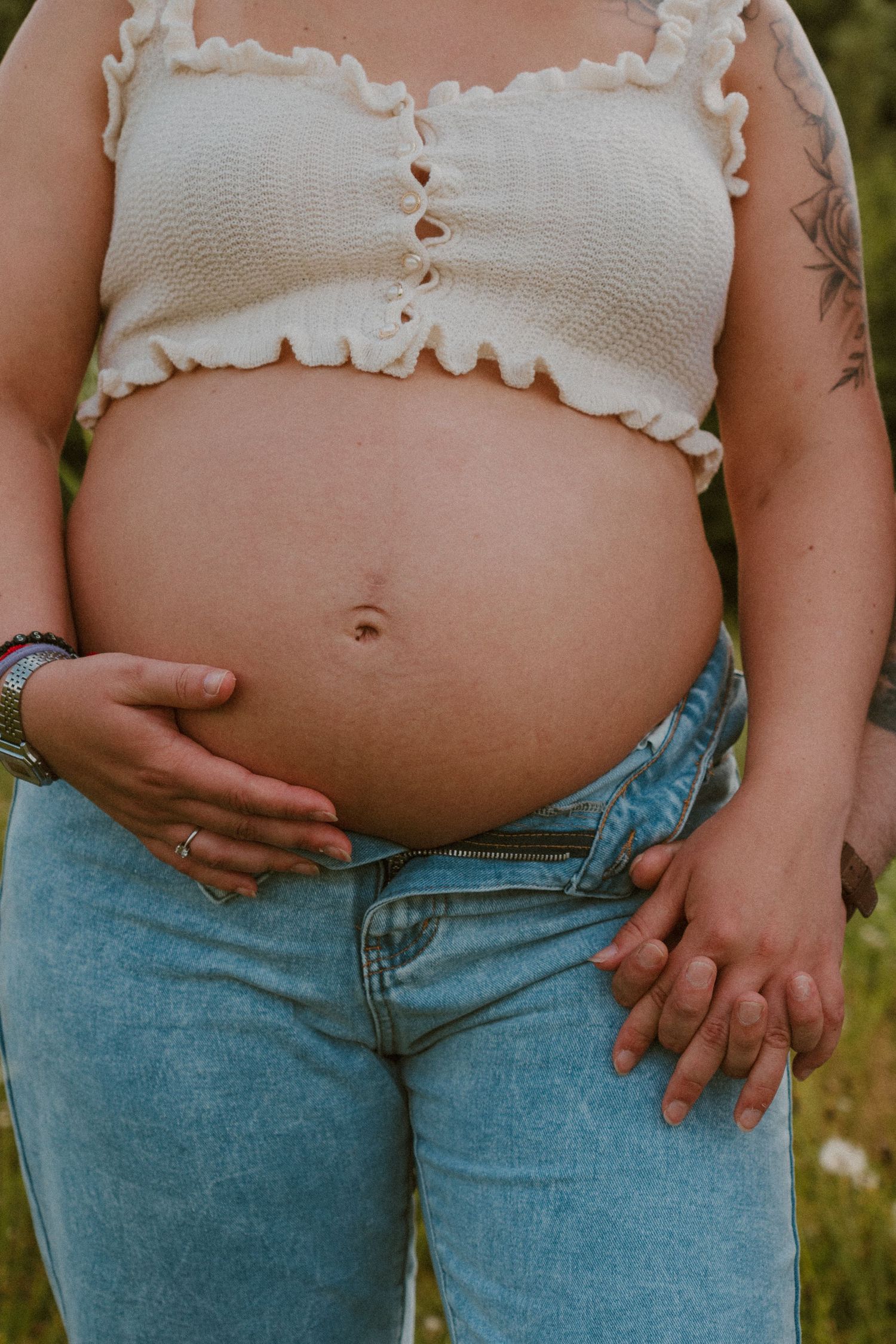 Four progressive pregnancy photos showing a growing baby bump in jeans and white top against a natural outdoor background.