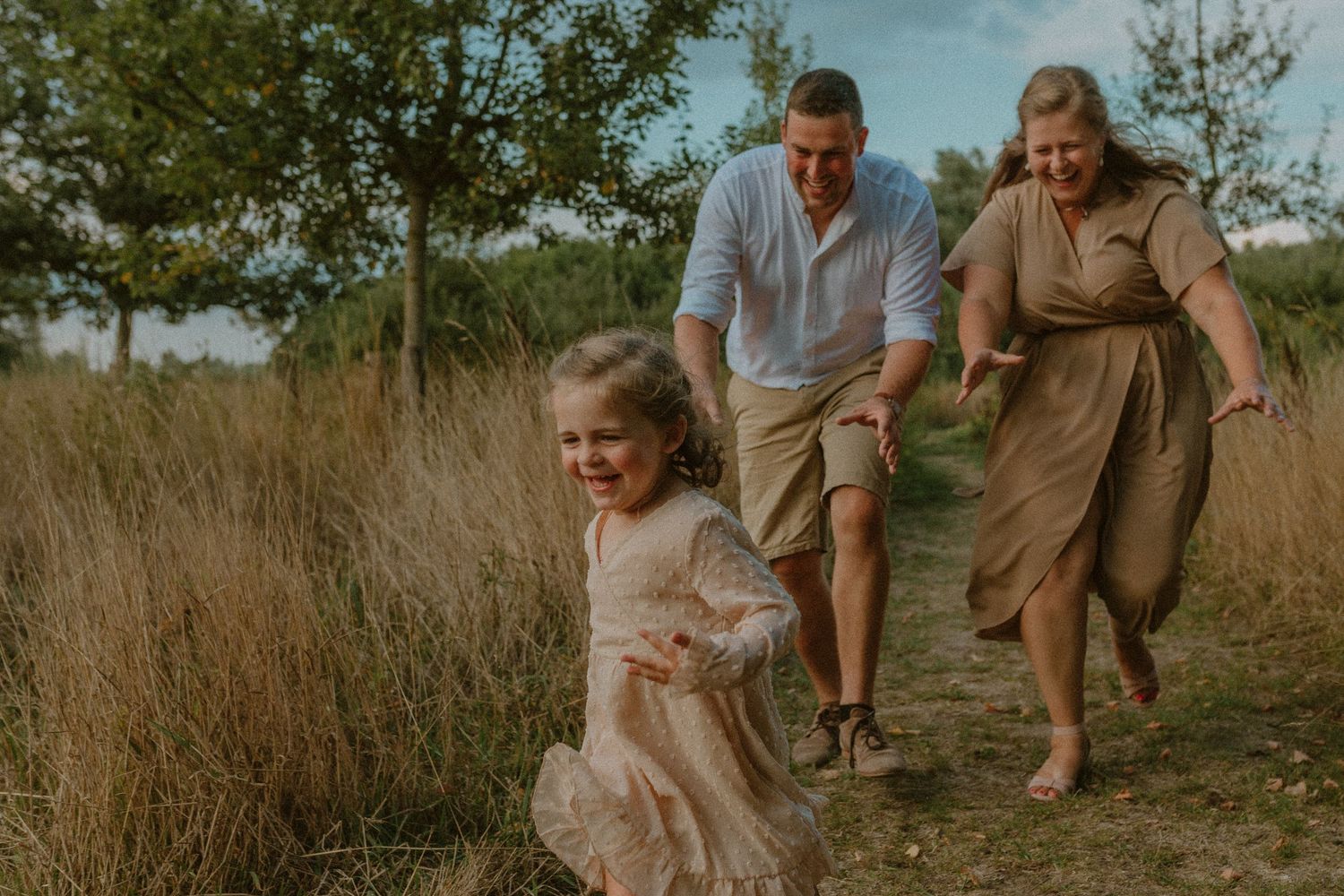 A family plays and laughs together in a golden wheat field during sunset.