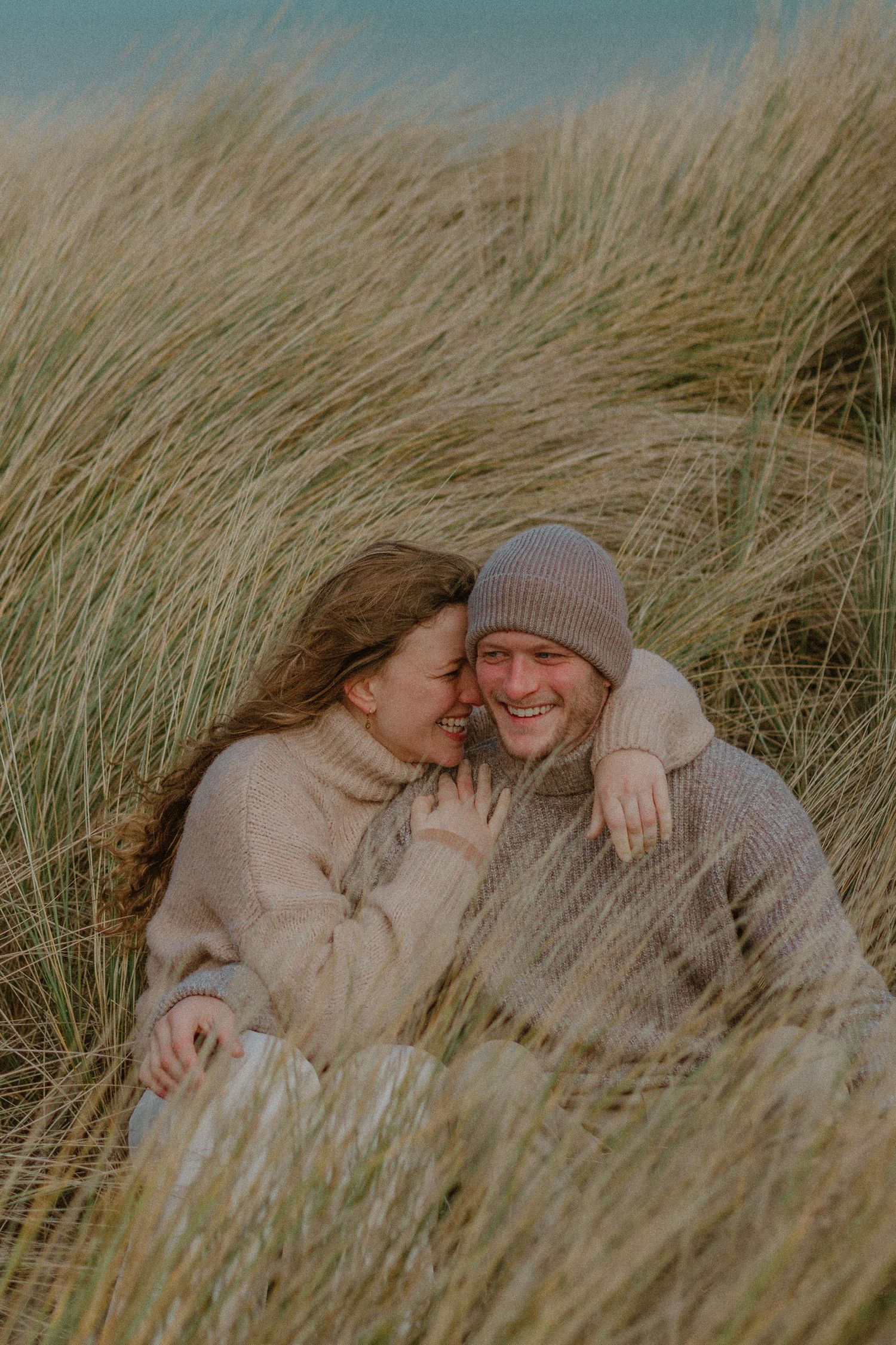 A couple shares an intimate moment while lying together in tall grass on a sunny autumn day.