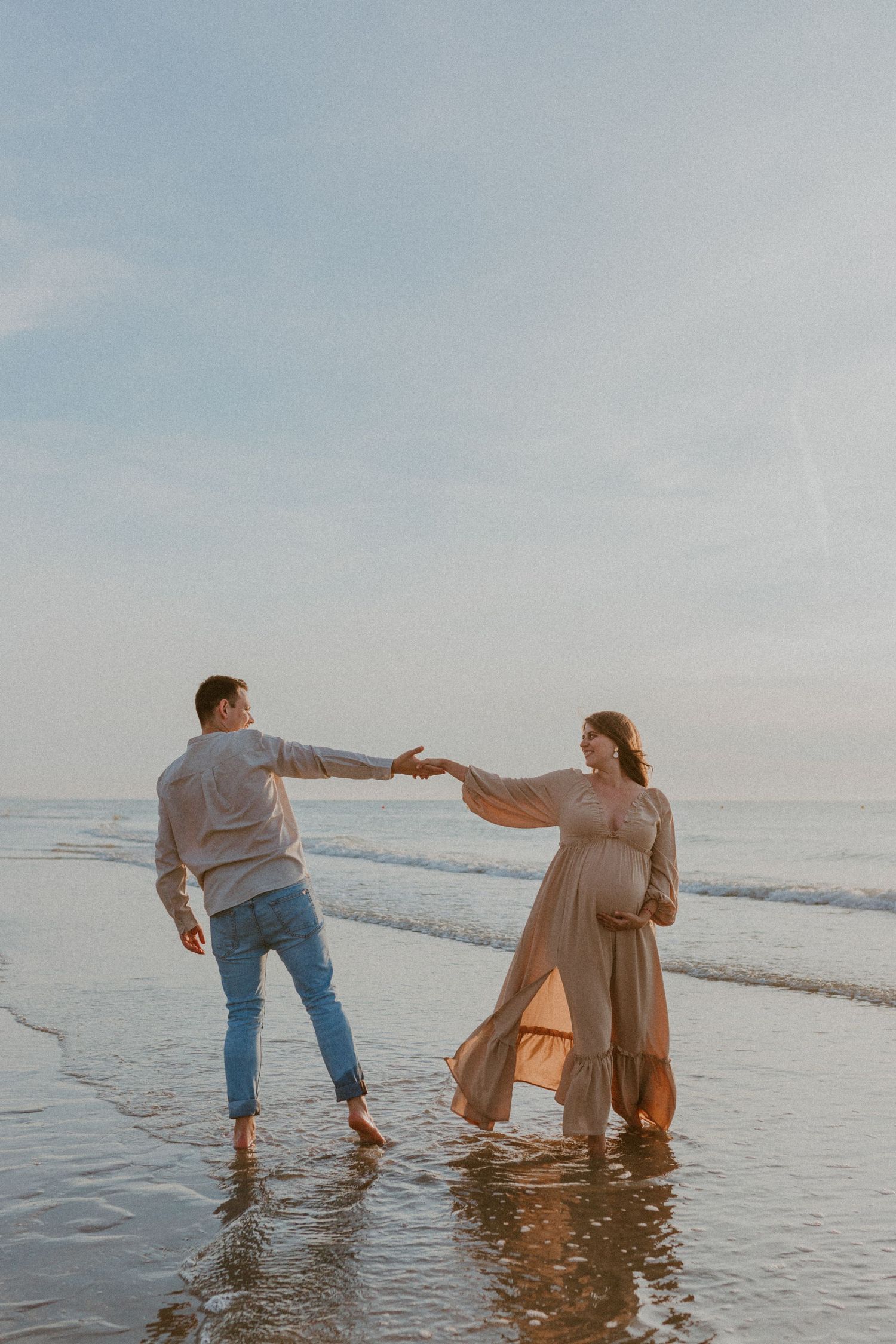 A couple holding hands and splashing in the ocean waves at sunset, creating a romantic beach scene.