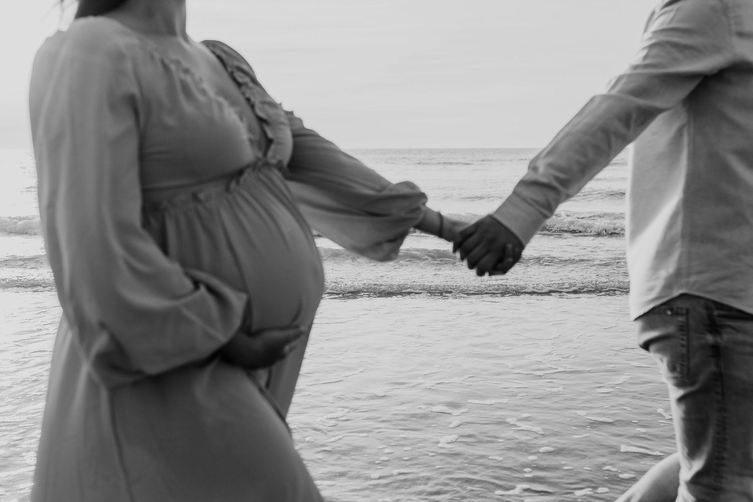 A couple walks along the beach at sunset holding hands while waves crash against the shore.