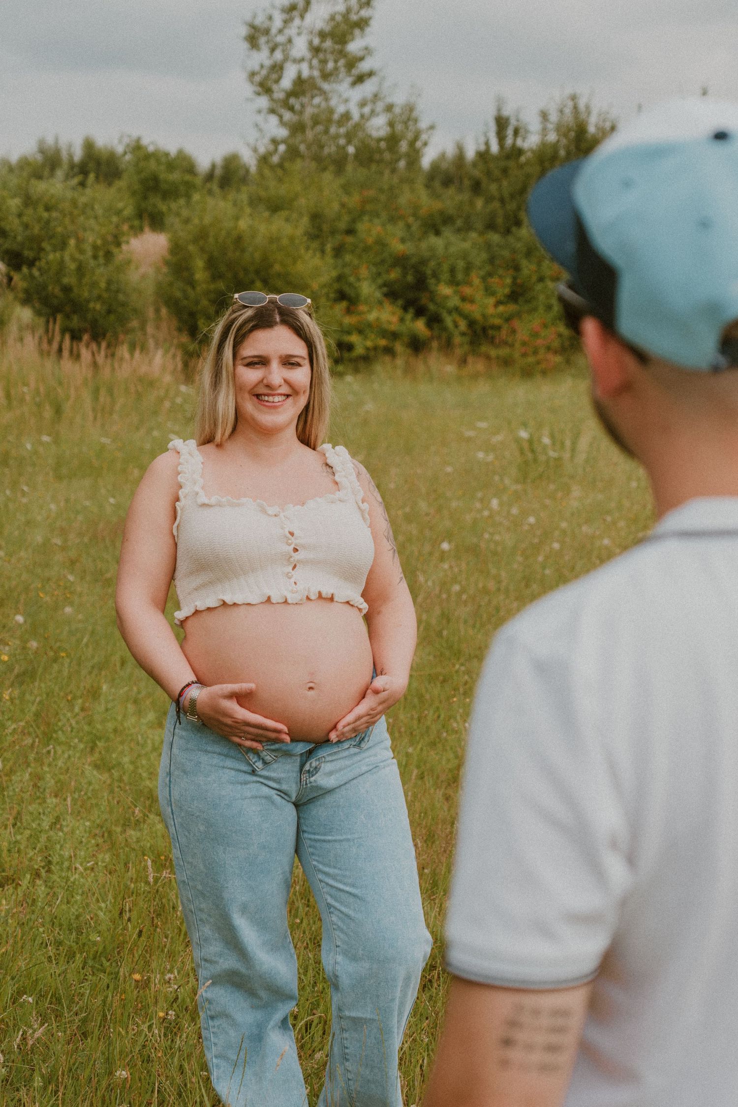 A series of candid maternity photos showing a couple in a sunlit meadow with light blue jeans and casual attire.