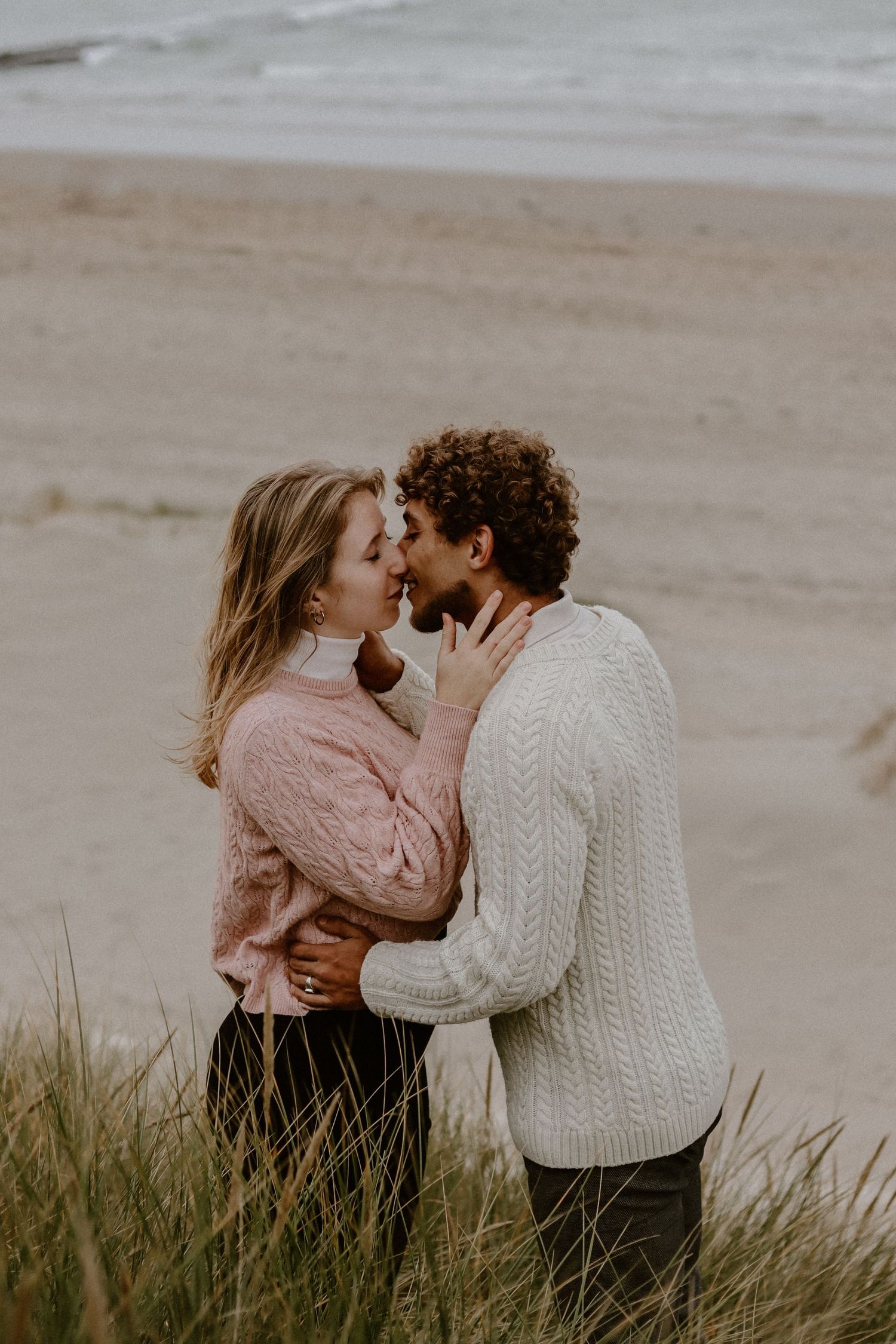 Een teder moment tussen een koppel op het strand, met duingras op de voorgrond.