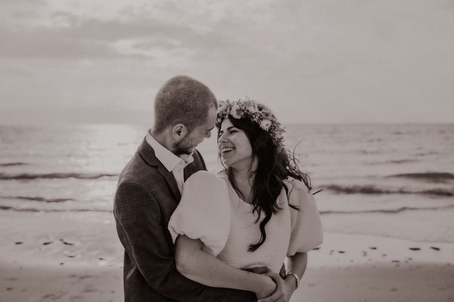 A romantic black and white photo series of a couple embracing on a beach at sunset.