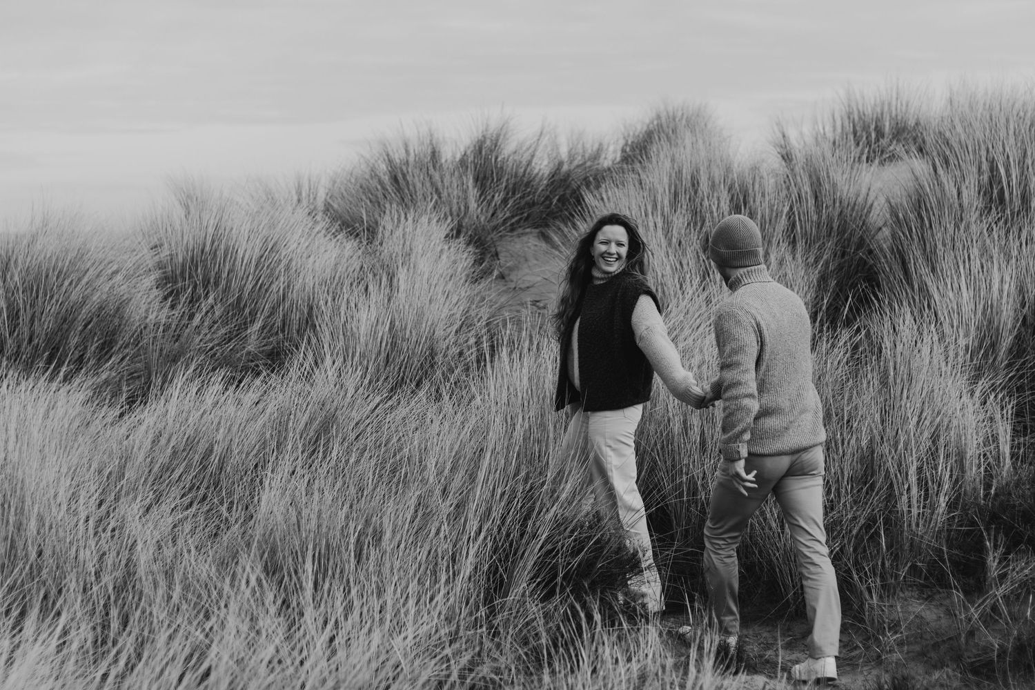 Black and white photo series shows people walking through tall grass in a field during a nature exploration.