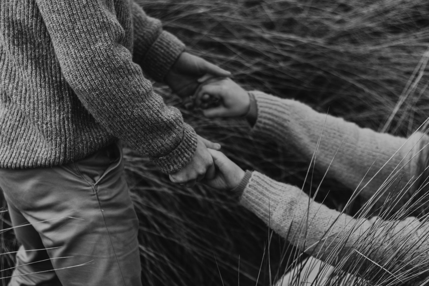 Person wearing a gray sweater reaches to touch a textured stone surface with their fingertips.