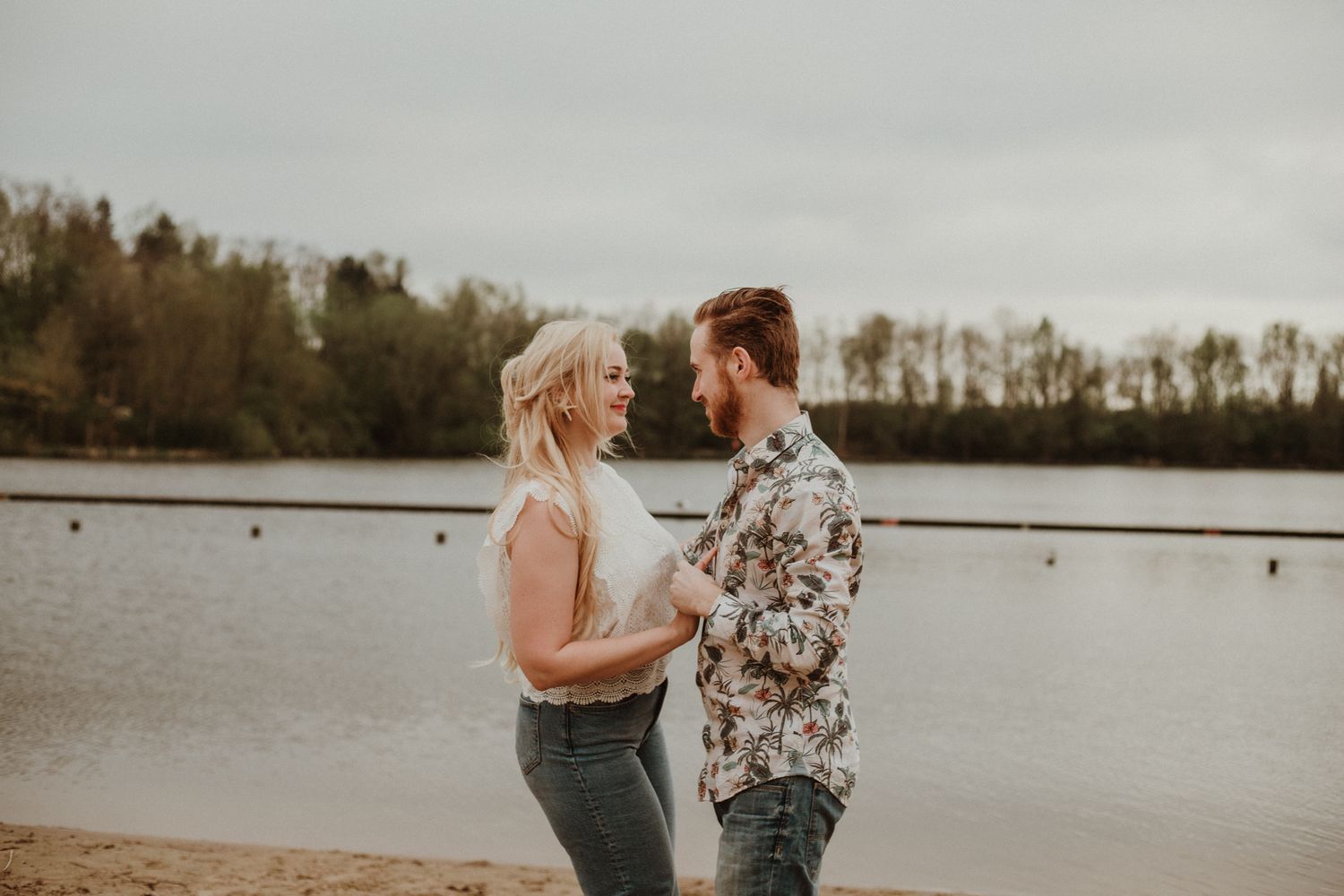 A couple shares an intimate moment by a serene lake during golden hour.