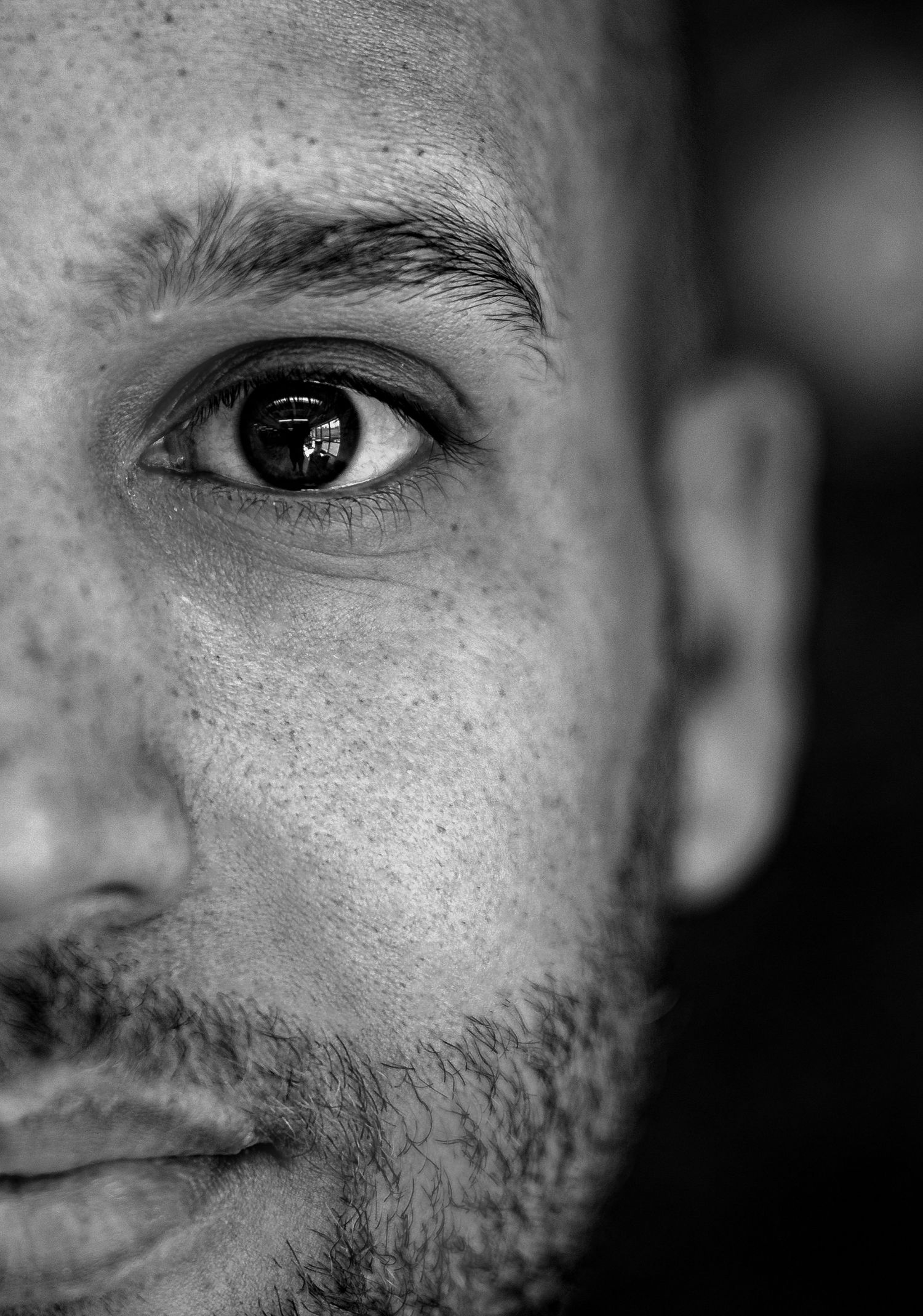 Close-up black and white portrait of a man with stubble, focused on one intense eye and facial details.