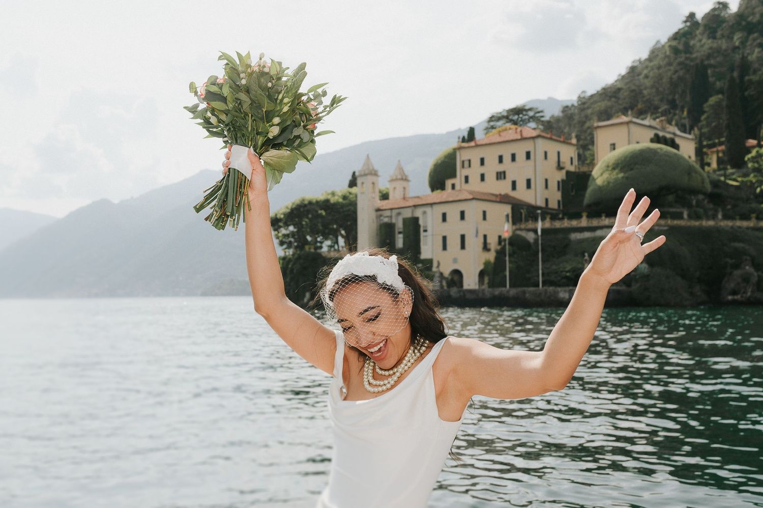 Bride celebrating on a boat in front of Villa del Balbianello during a luxury destination wedding on Lake Como
