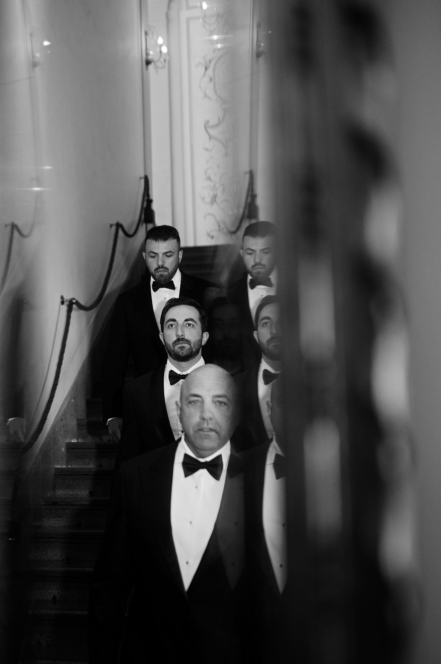 Groom and groomsmen descending a staircase, captured in black and white with a cinematic and editorial style