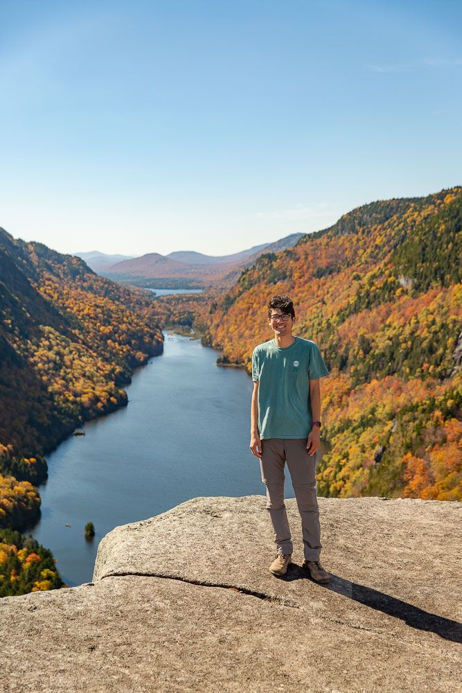 Man posing for a picture at the viewpoint for Indian Head Trail in Keene Valley, New York during the fall foliage
