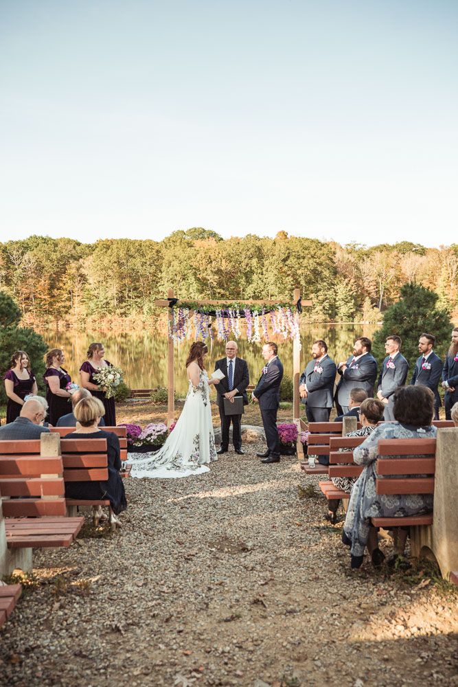 Couple exchanging vows during their fall wedding ceremony at June Norcross camp in Ashford, CT captured by illuminate the stars Photography