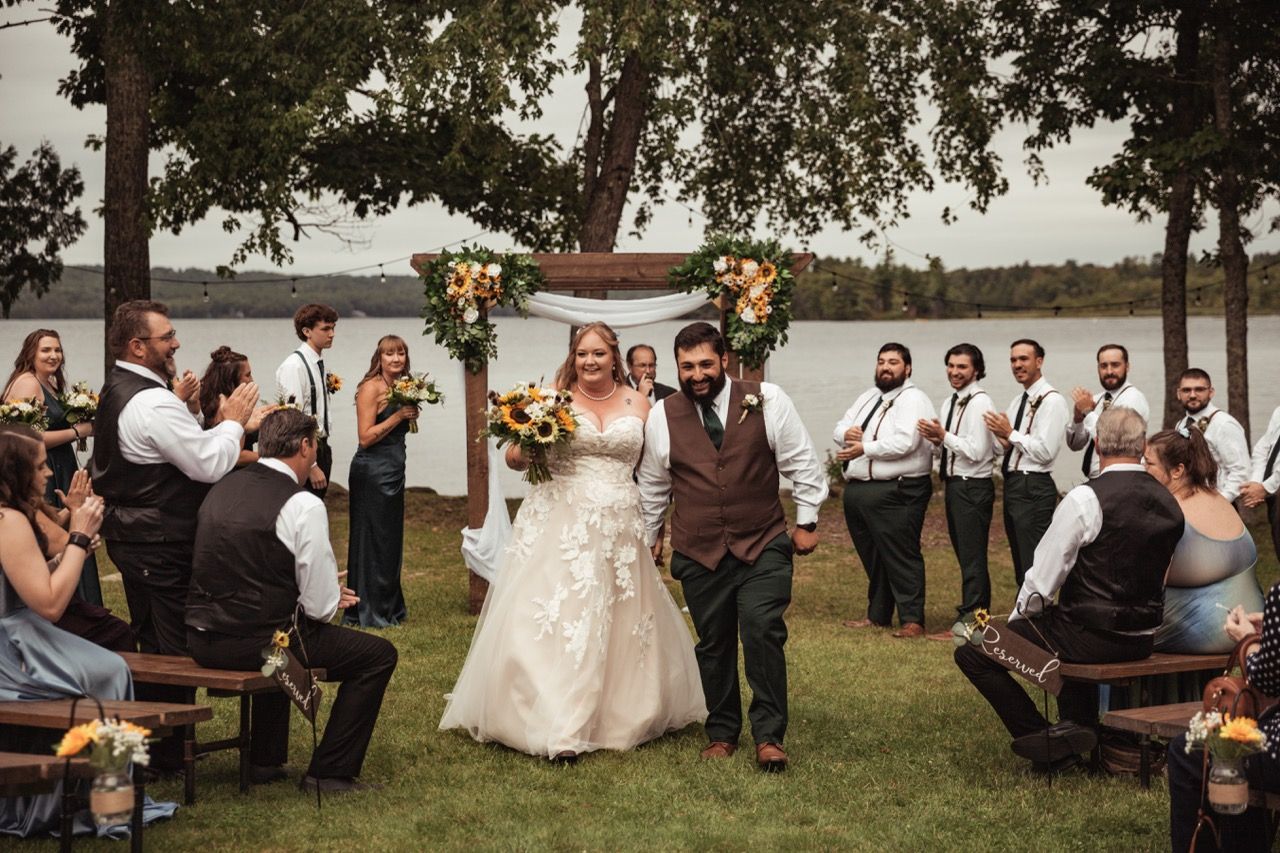 Couple exits down the aisle after fall wedding ceremony at The Lakeside Lodge in Sydney, Maine captured by illuminate the stars Photography