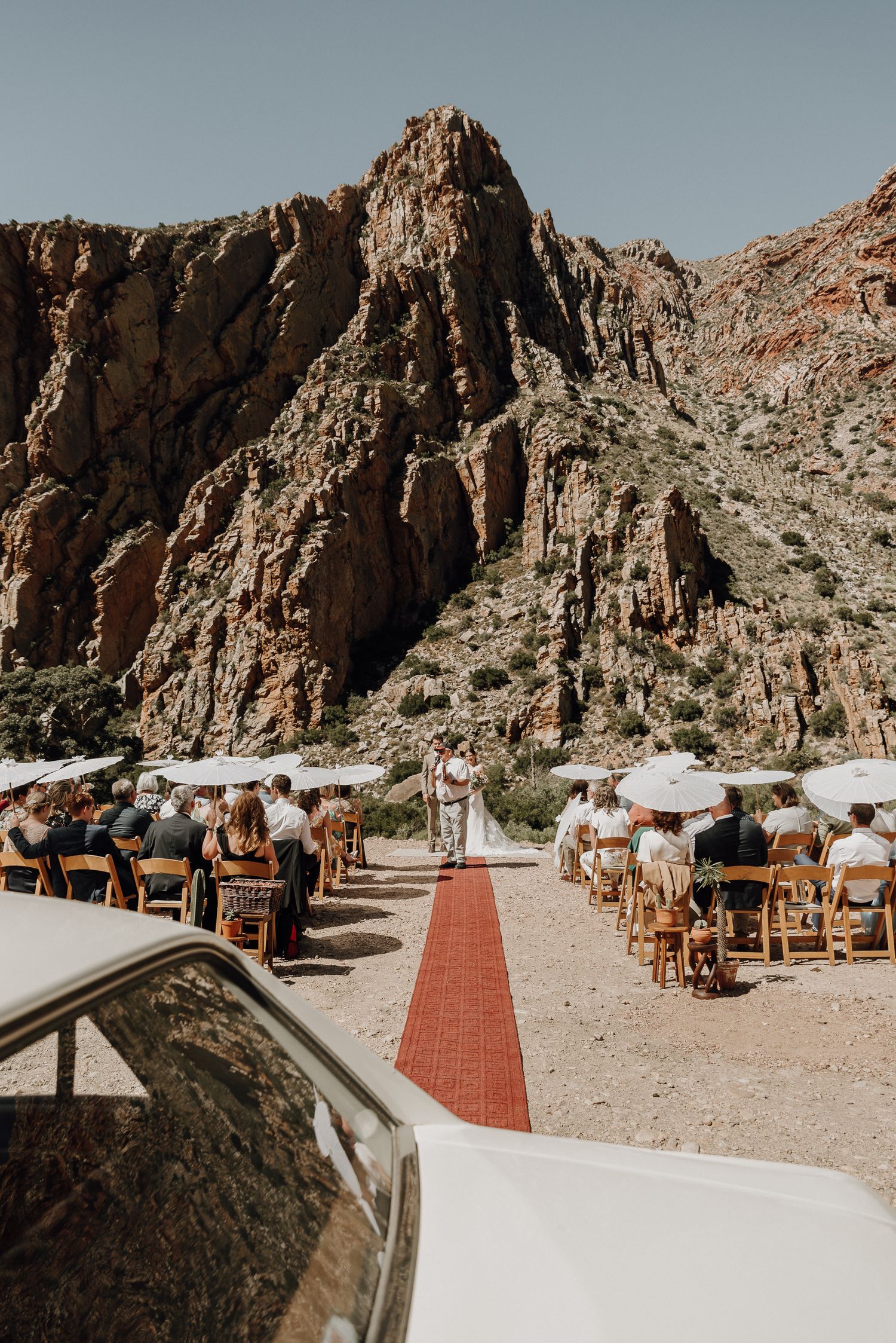 Wedding car in foreground reflecting sandstone cliffs of Swartberg Mountains with Prince Albert destination wedding ceremony at Eerstewater