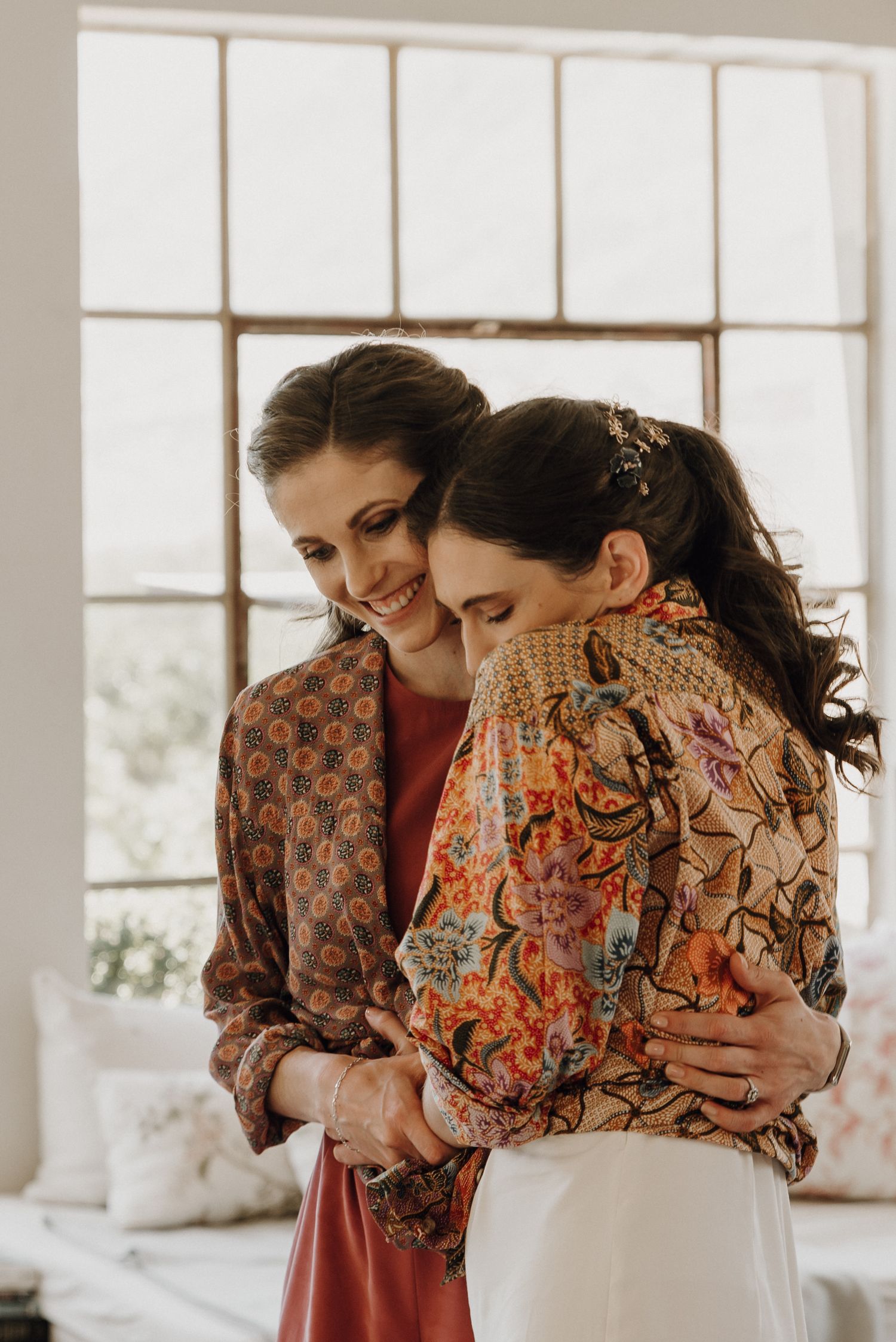 Bride and her sister hugging while wearing their mother's old blouses before getting ready for this Prince Albert destination wedding