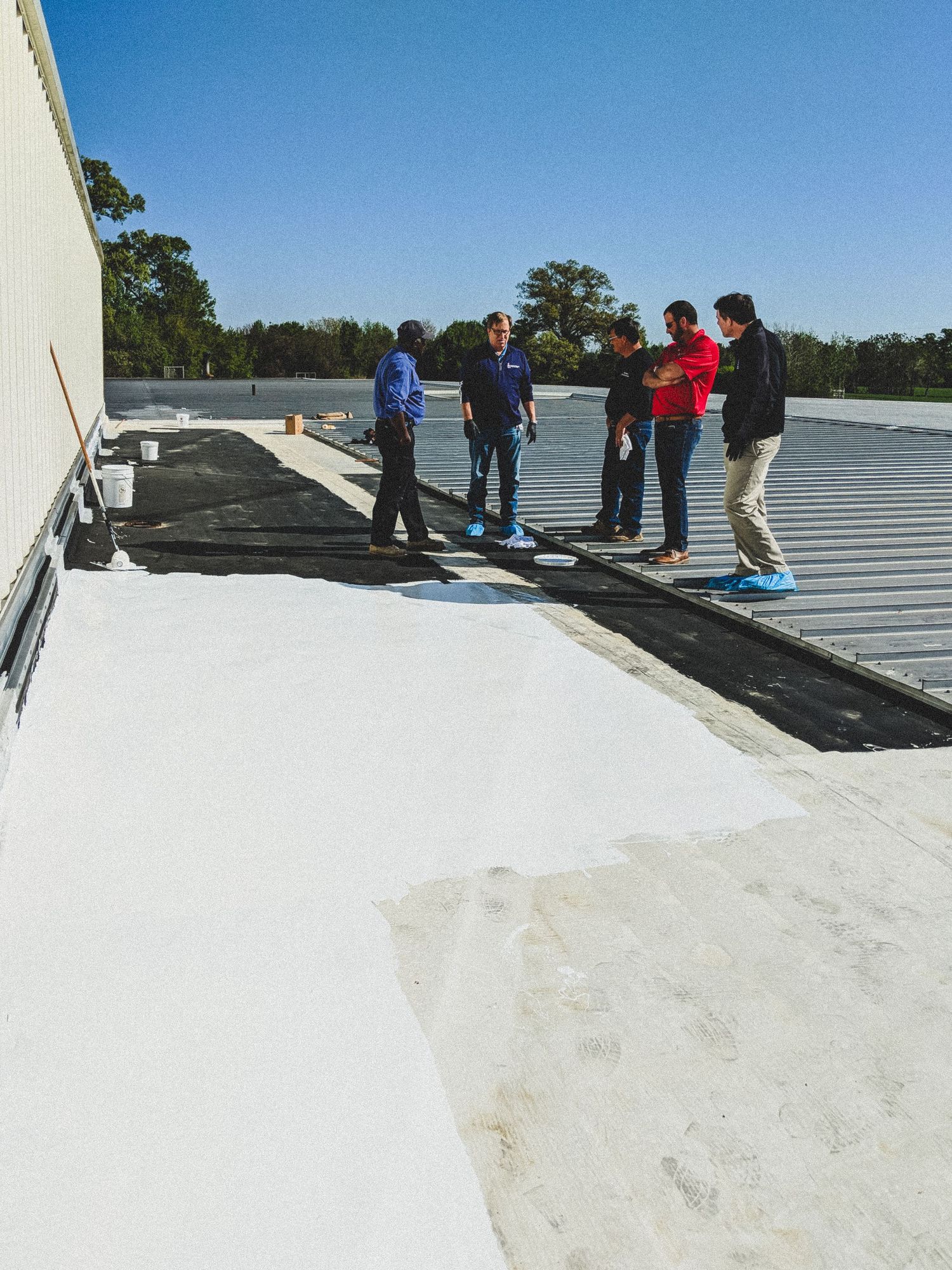 On-site Video Production inspecting a commercial flat roof with white and black surfaces on a sunny day.