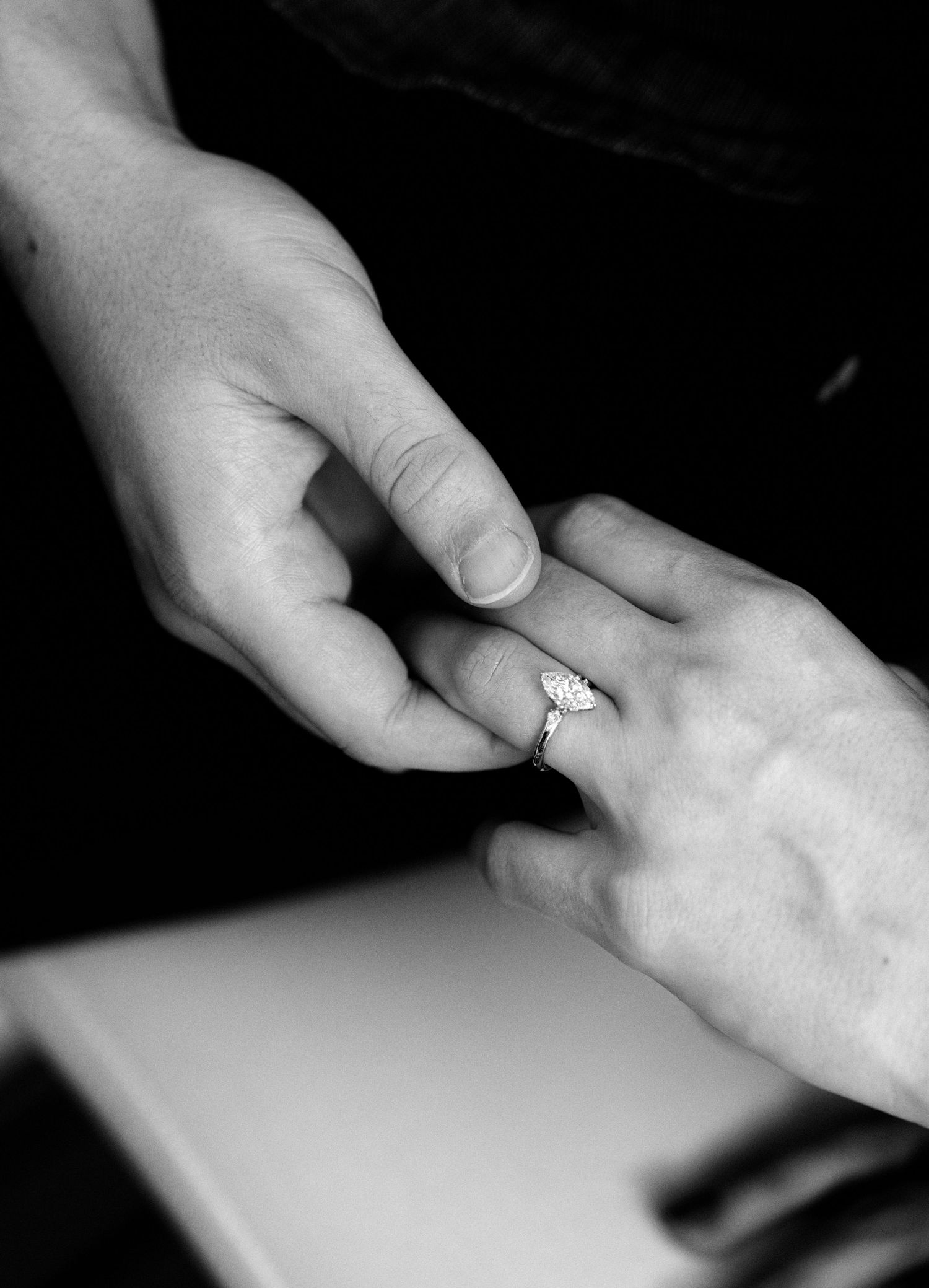 Close-up black and white photo of engagement ring being placed on woman's finger.