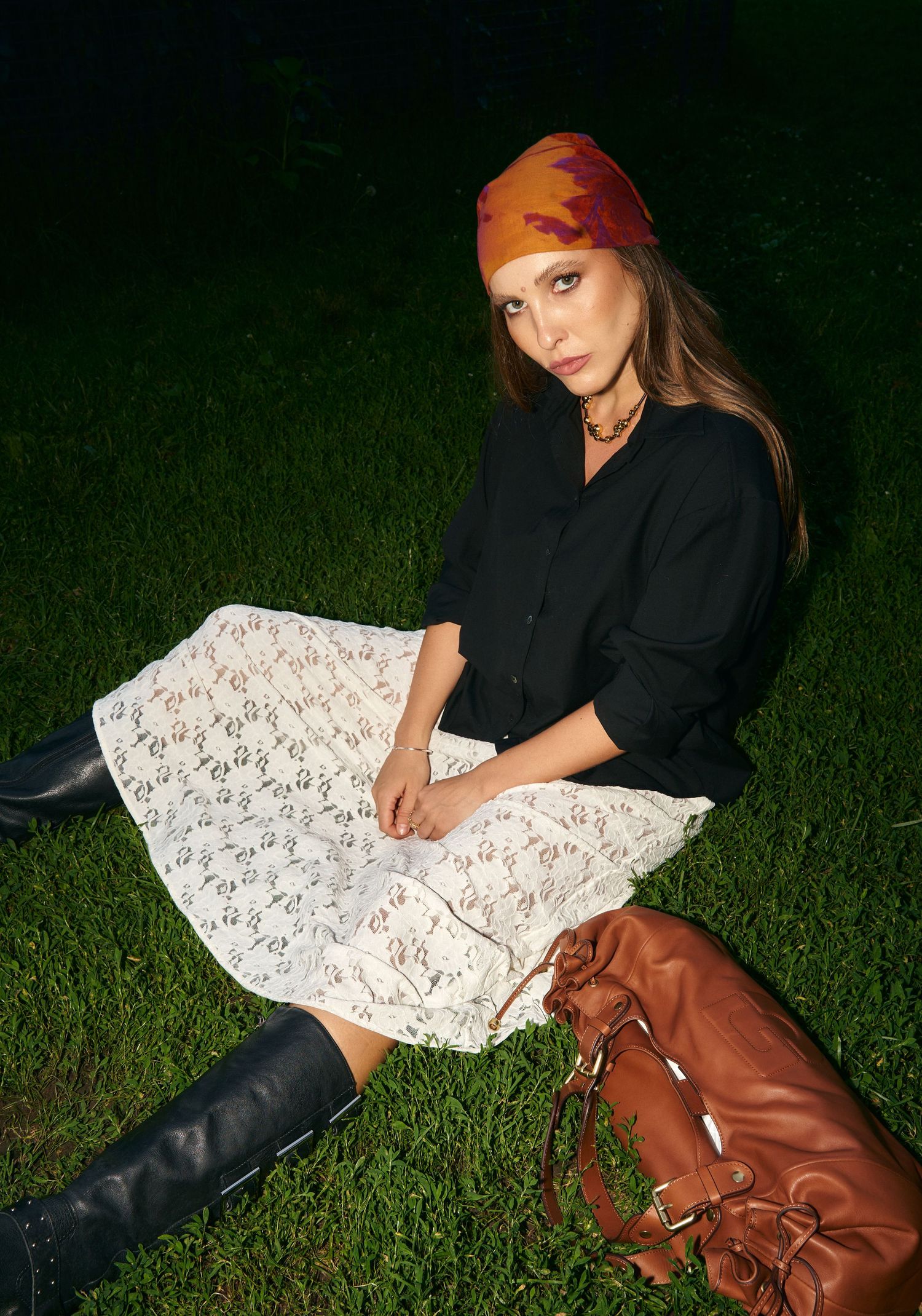 A woman in a black top, lace skirt, and headscarf sits on grass at night.