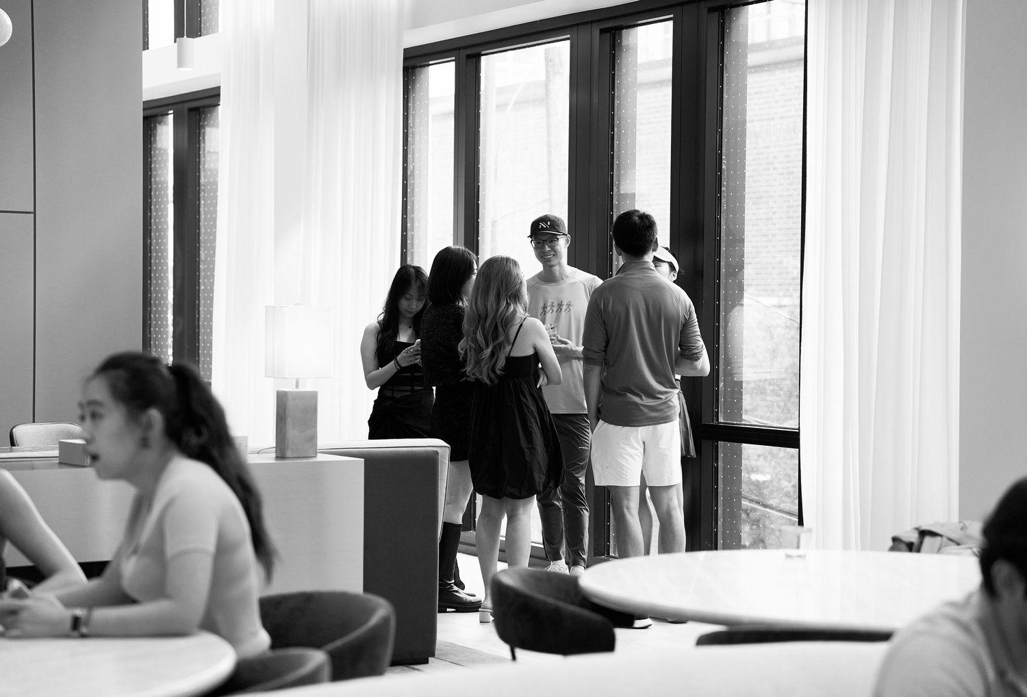 Group of young people gathered by large windows in modern interior space.