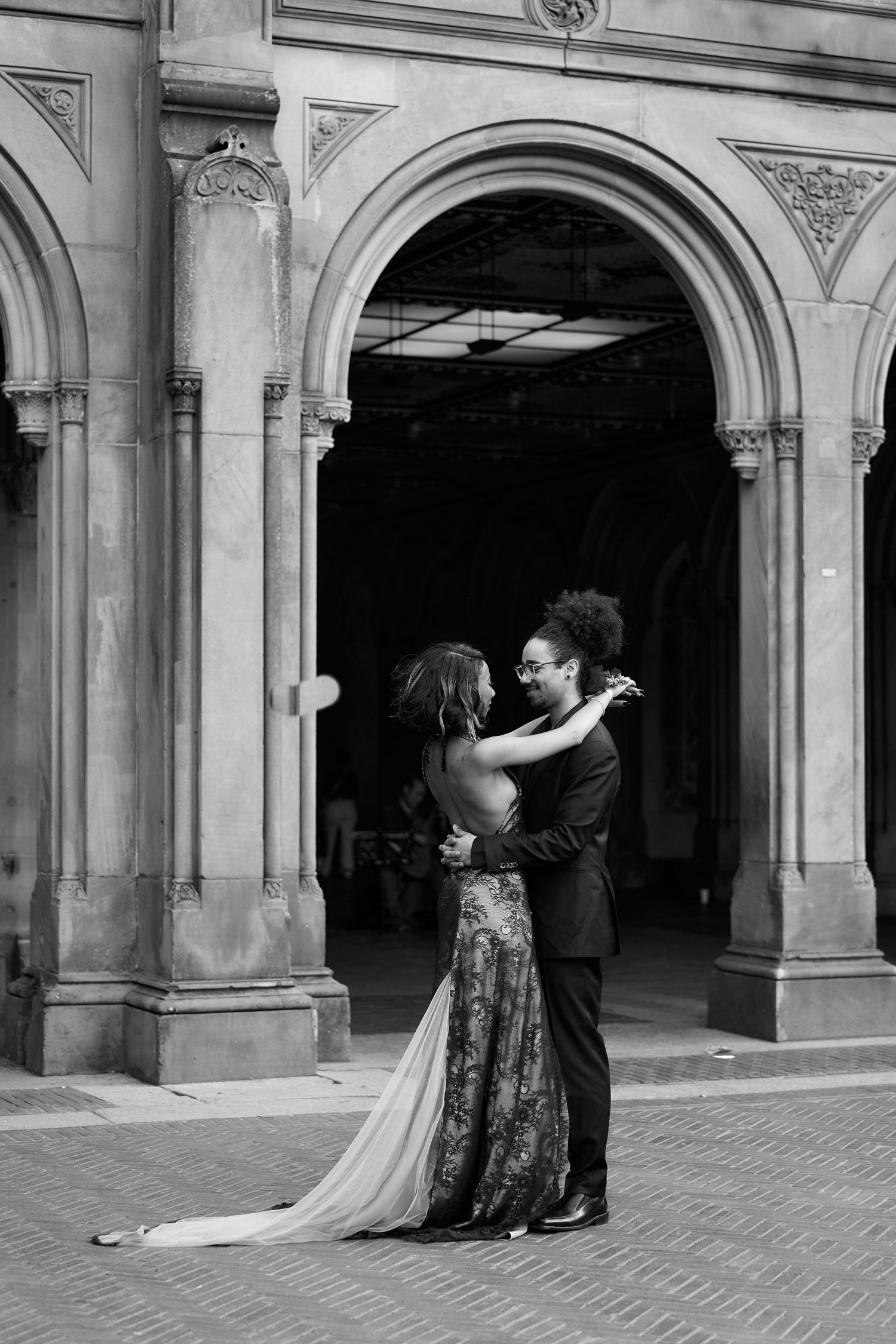 Black and white photo of couple embracing under arched columns at Bethesda Terrace, Central Park.