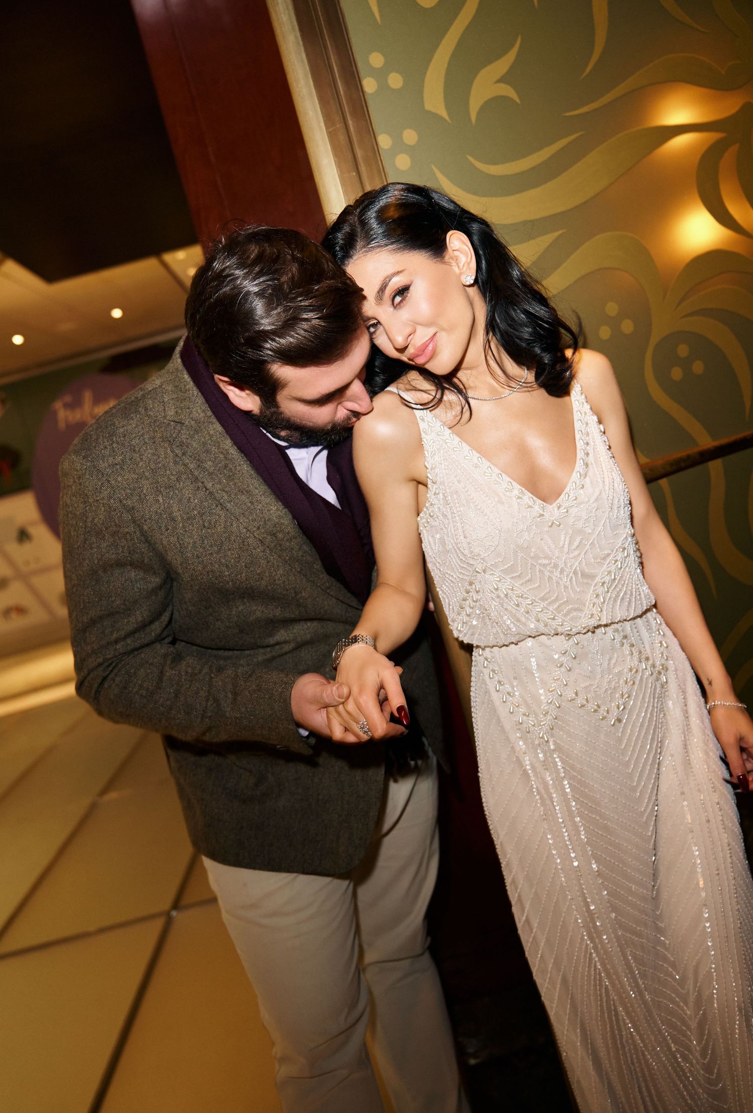 Couple sharing a romantic moment, man in tweed blazer whispering to woman in beaded white gown.