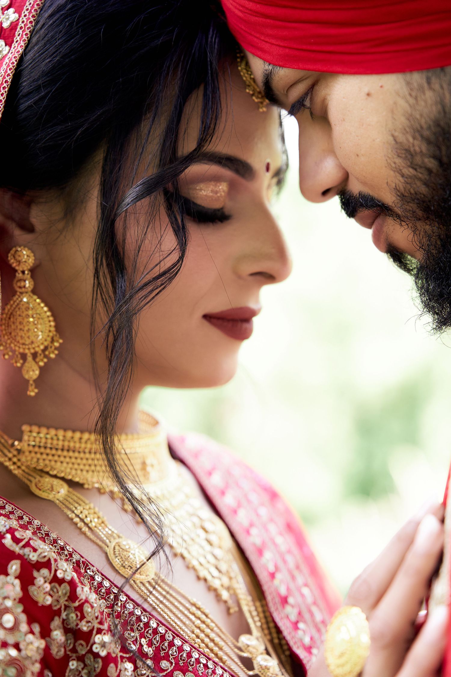 Indian bride and groom in traditional red wedding attire sharing intimate moment outdoors.