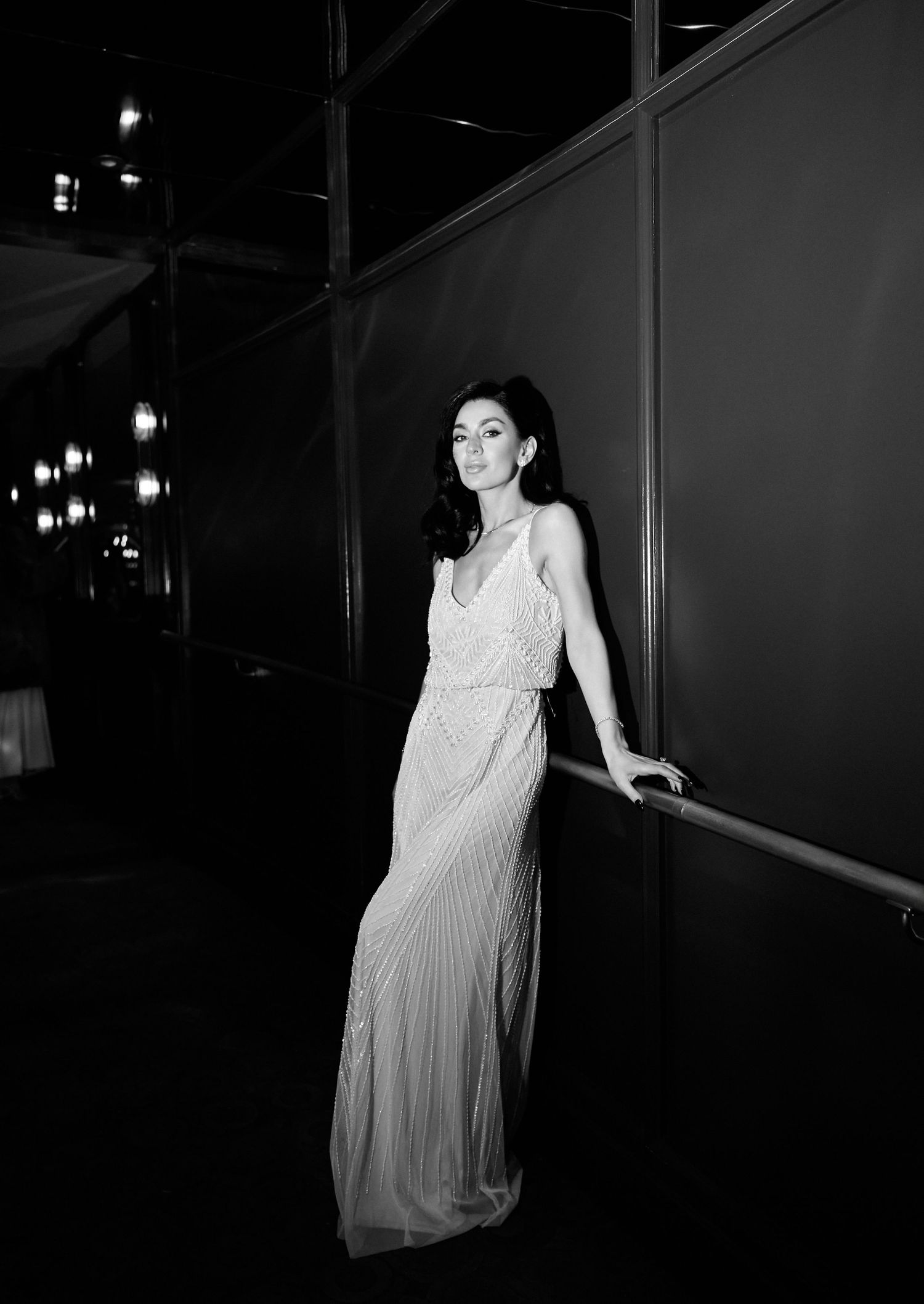 Elegant woman in beaded white gown posing in dimly lit hallway in black and white photography.