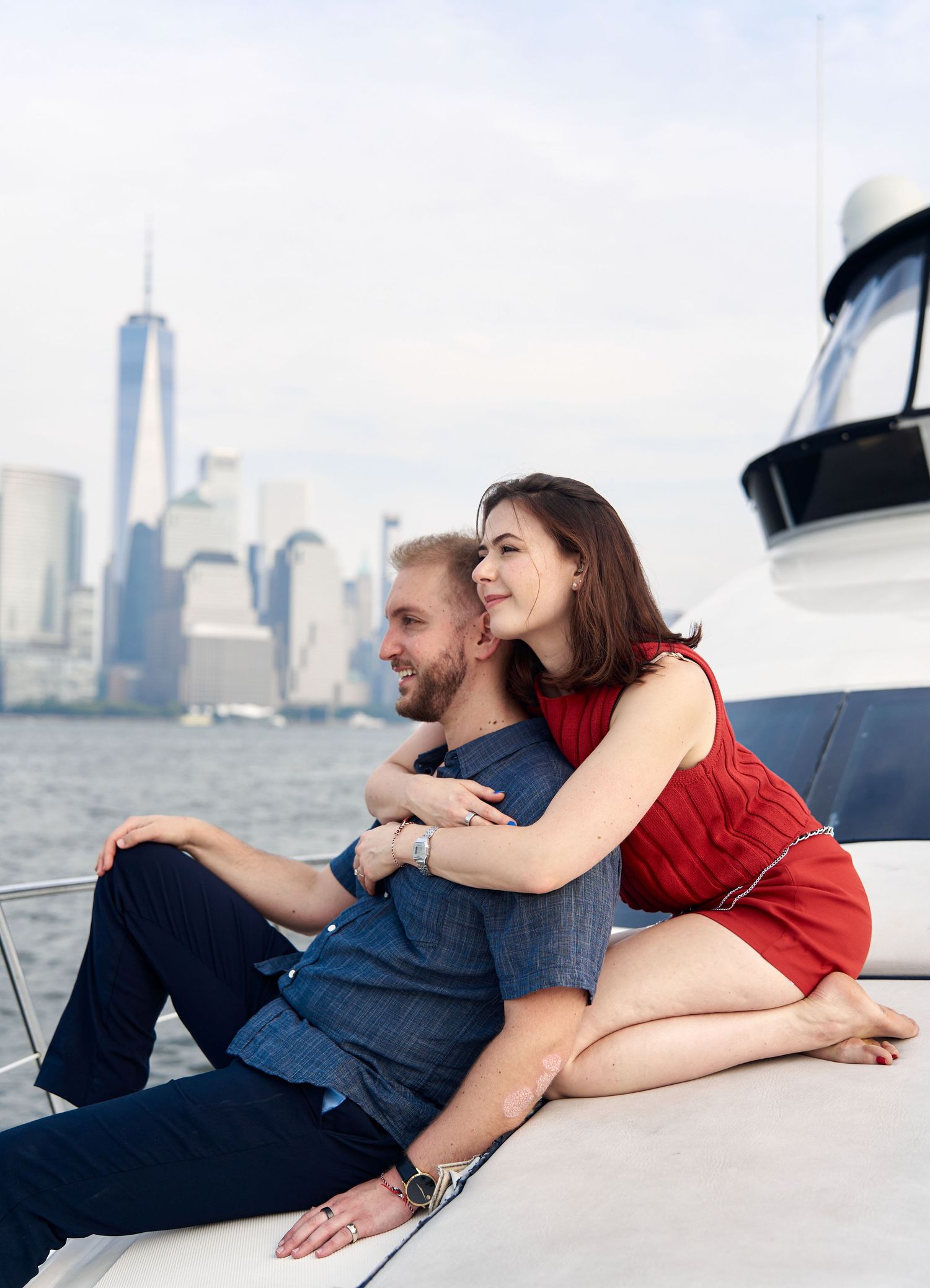 Couple embracing on yacht deck with One World Trade Center skyline view.