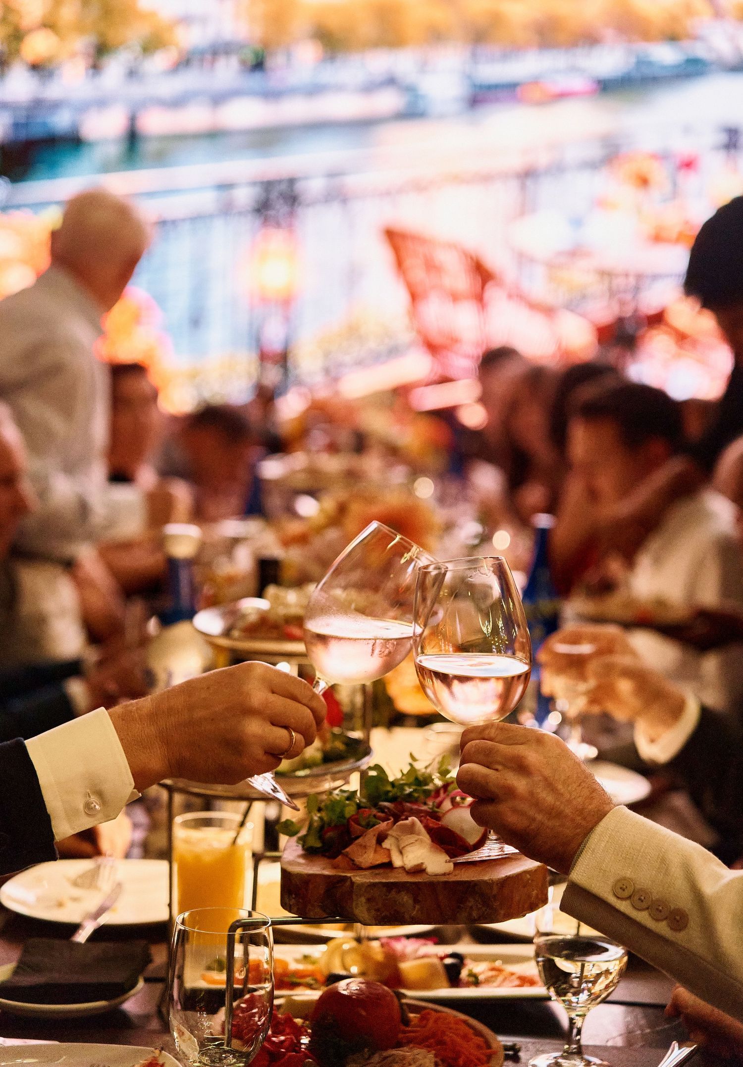 Two people toasting with white wine glasses at a vibrant, festively lit dinner party event.